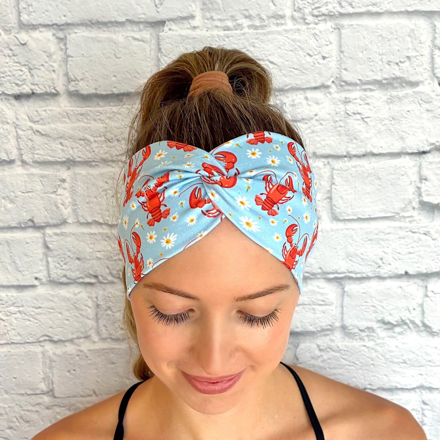 Woman with hair in ponytail wearing wide, twisted, light blue headband with lobster and white floral print.