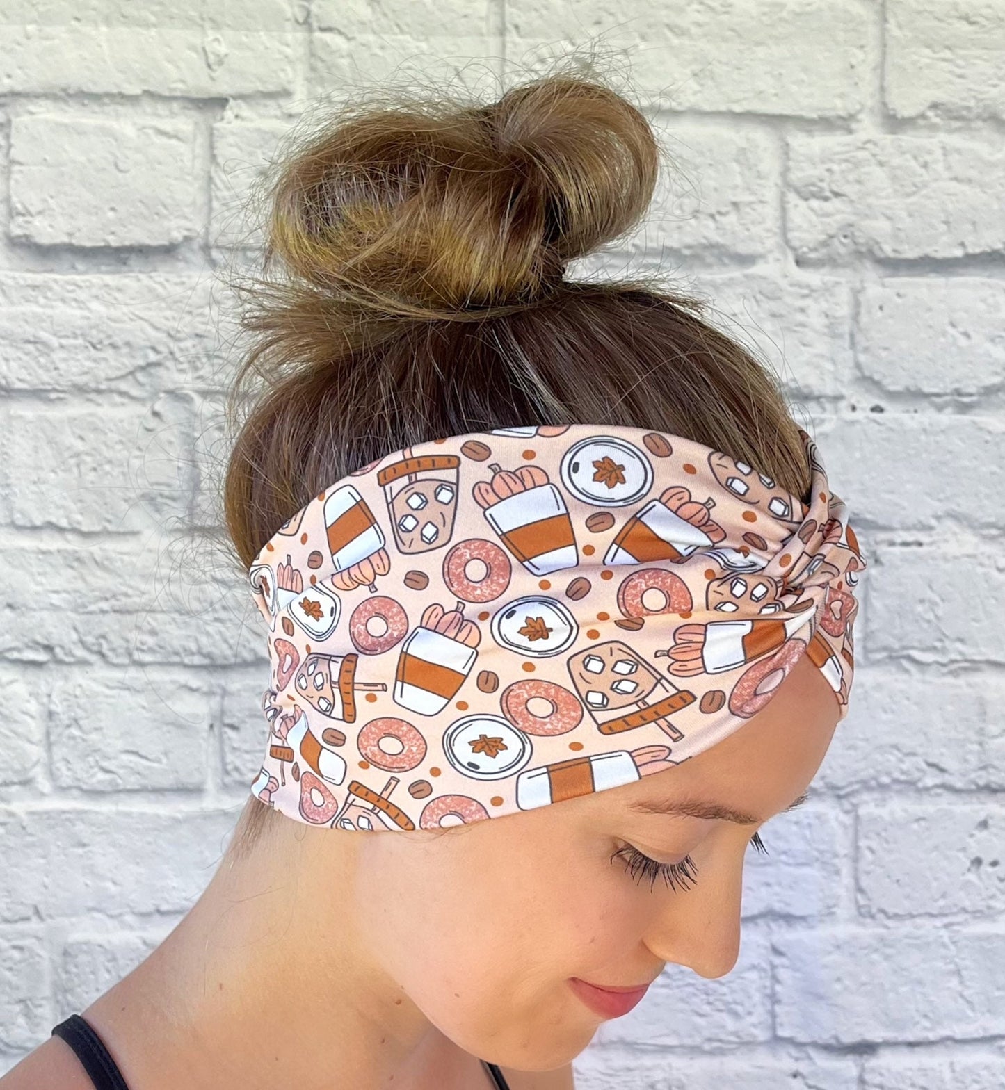 Woman wearing a fall theme, pumpkin spice patterned headband against a white brick wall
