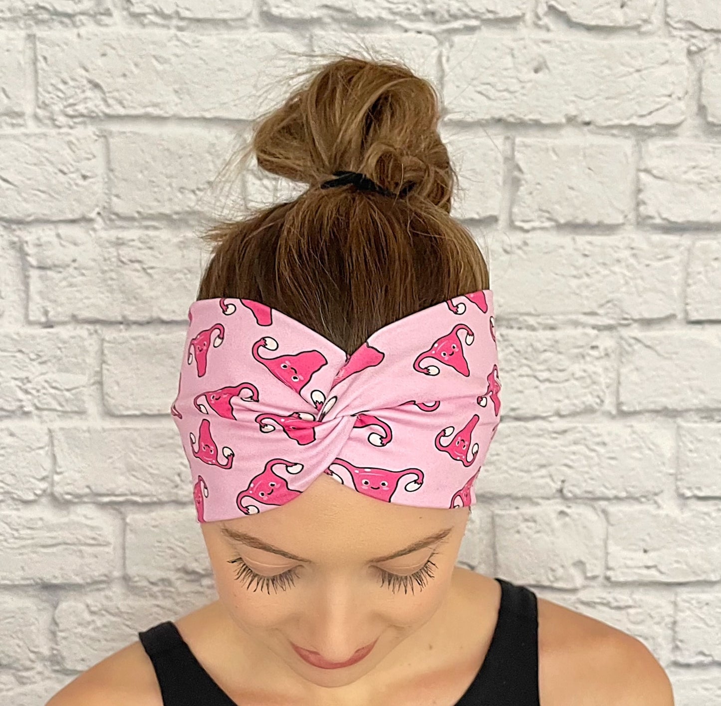 Woman with hair in bun wearing wide, twisted headband in light pink with dark pink uterus print.