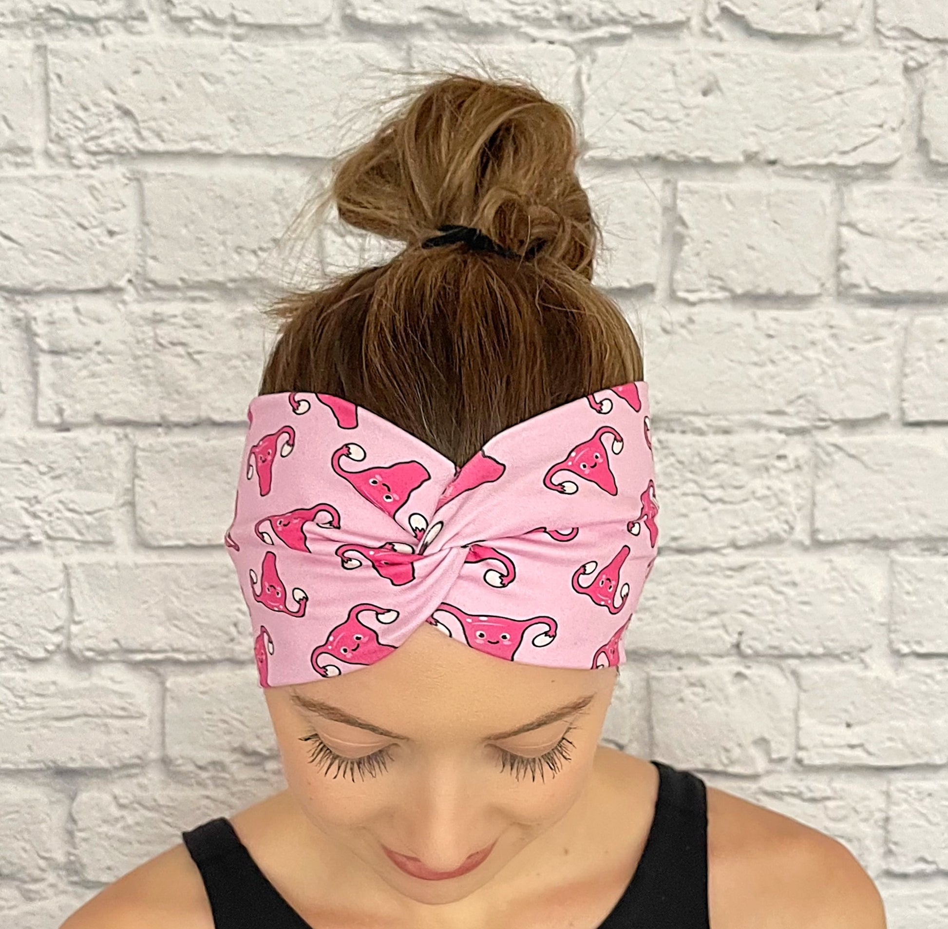 Woman with hair in bun wearing wide, twisted headband in light pink with dark pink uterus print.