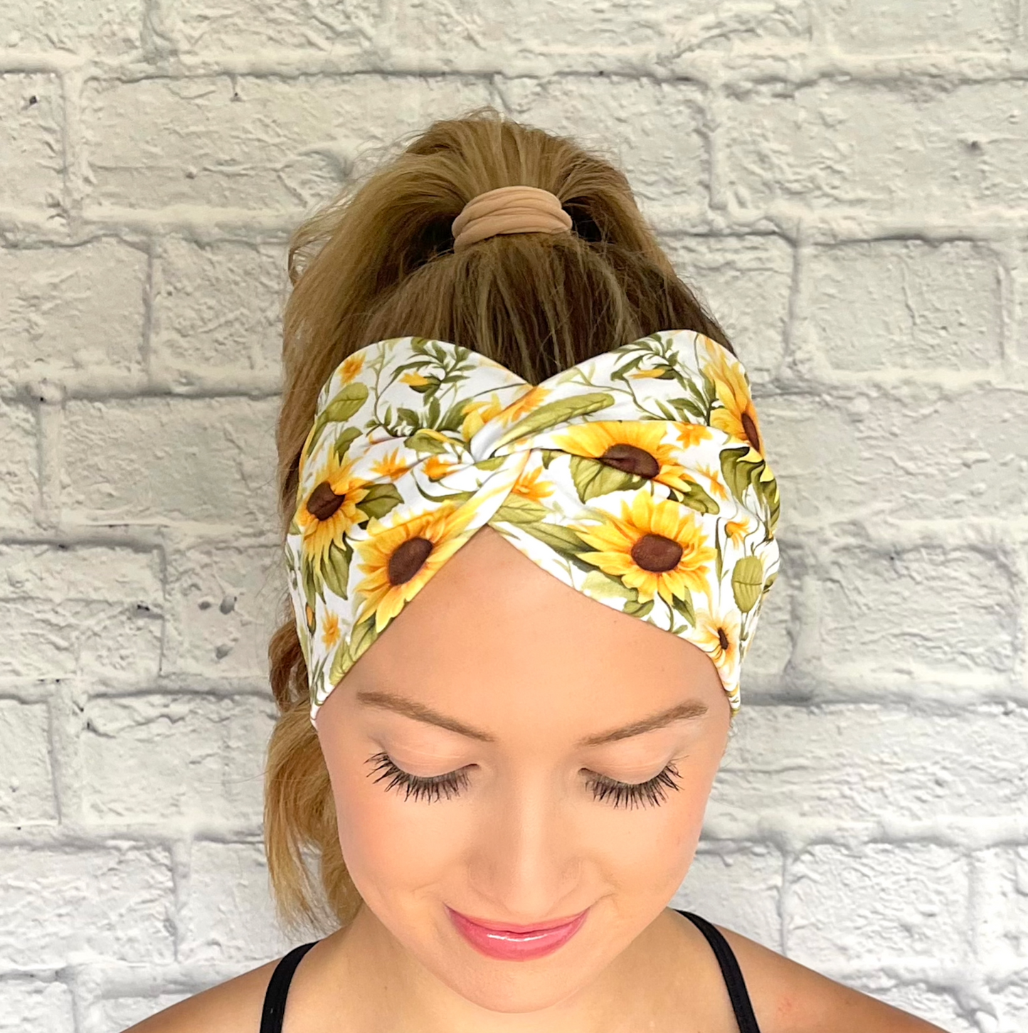 Woman with hair in ponytail wearing white, stretchy headband in white with yellow sunflower print.