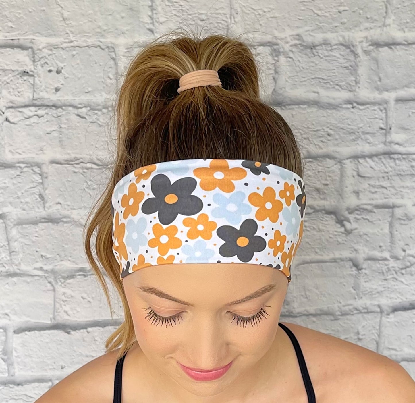 Woman with hair in curled ponytail wearing flat, stretchy headband in yellow, navy, and light blue floral print.