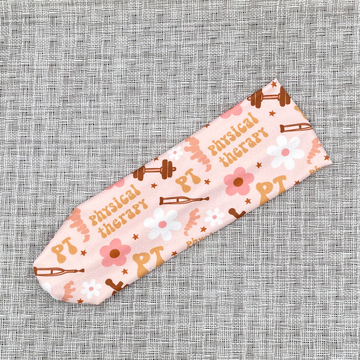 Light pink headband with print- PT, physcial therapy, flowers, crutches, a wheelchair, and weights.
