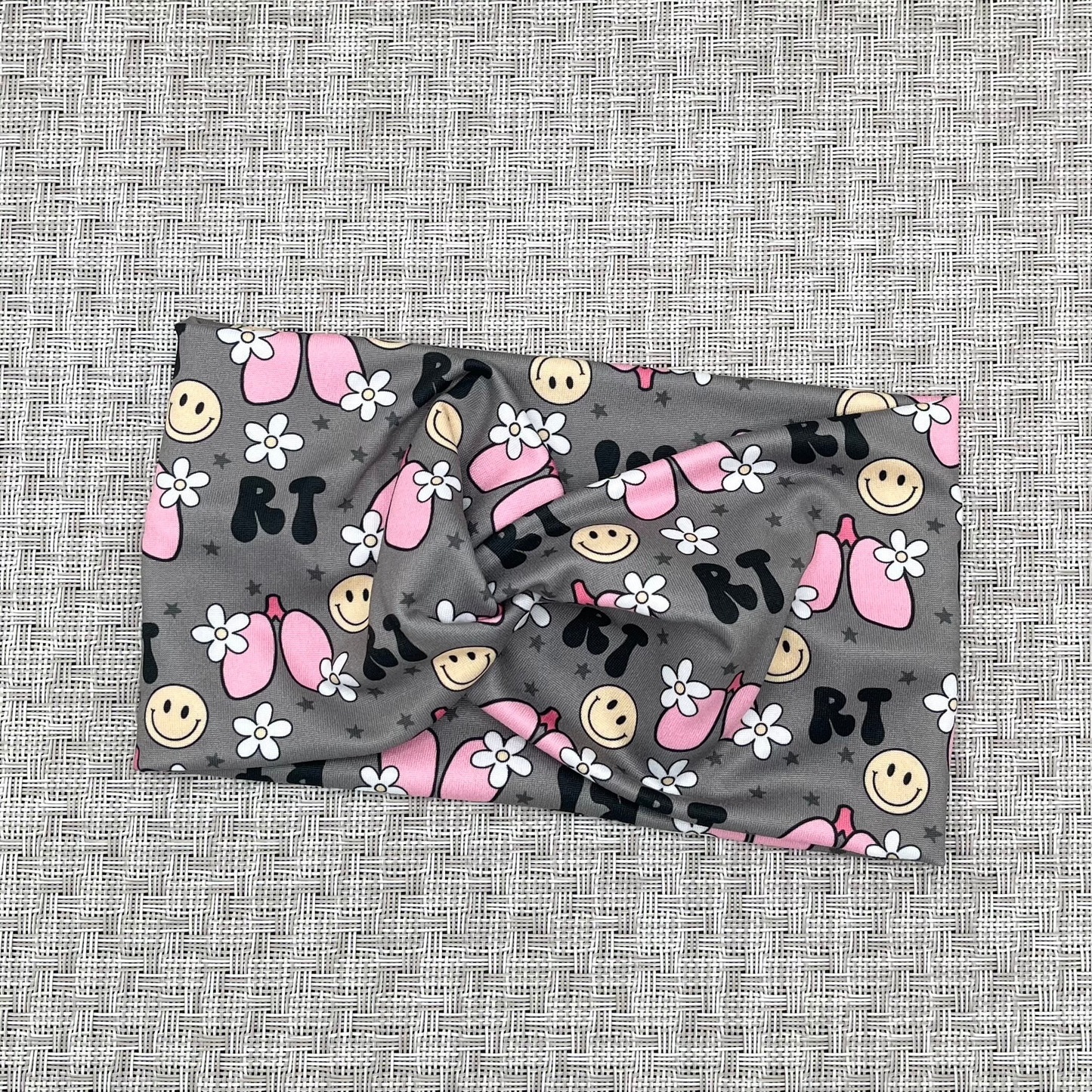 Wide, twisted headband in gray with "RT" print, lungs, flowers, and smiley faces.