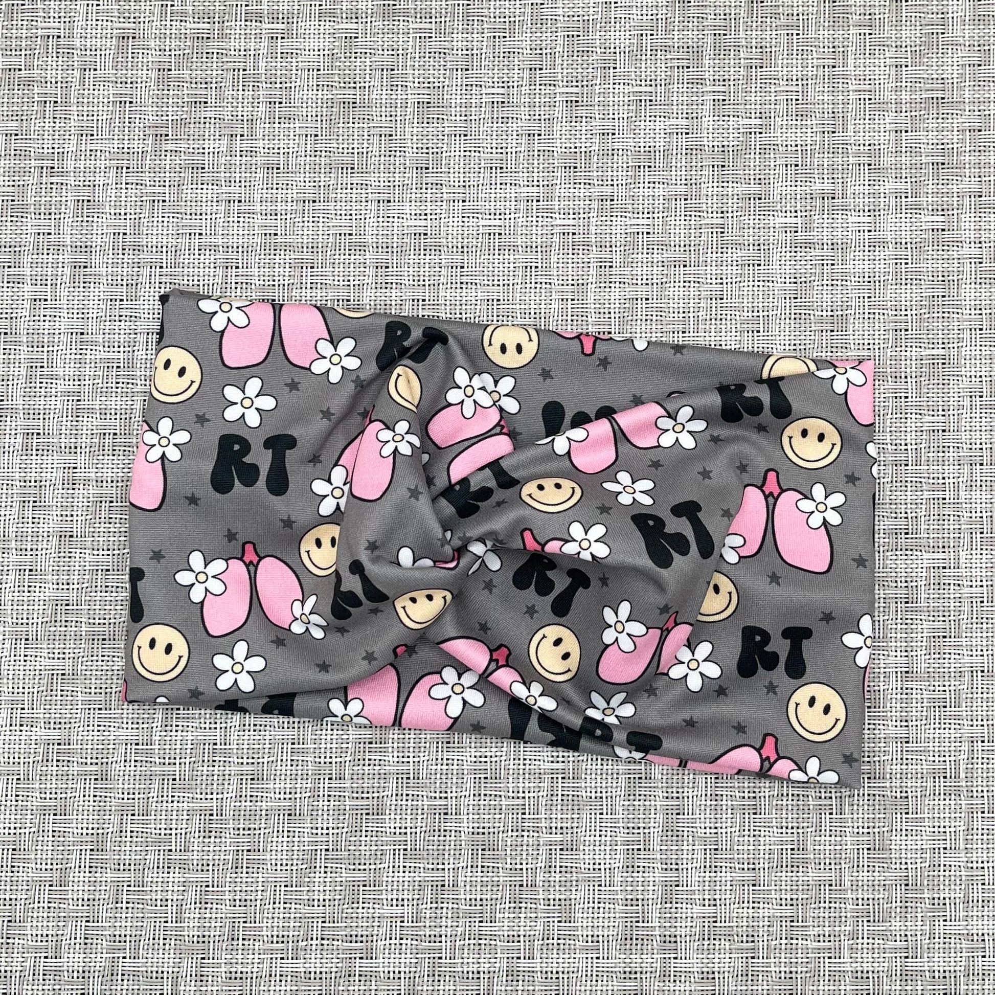 Wide, twisted headband in gray with "RT" print, lungs, flowers, and smiley faces.