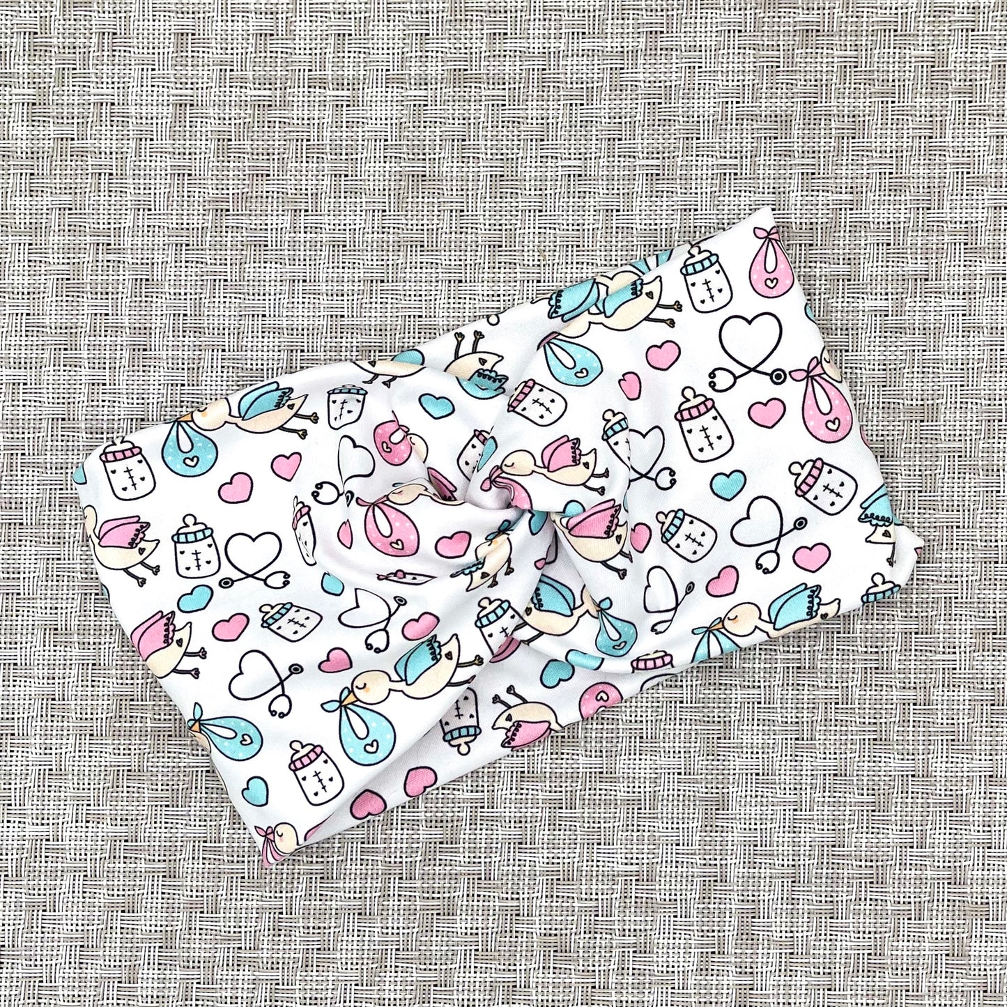 Wide, twisted headband in white with baby theme print- storks, hearts, bottles, and stethoscopes.