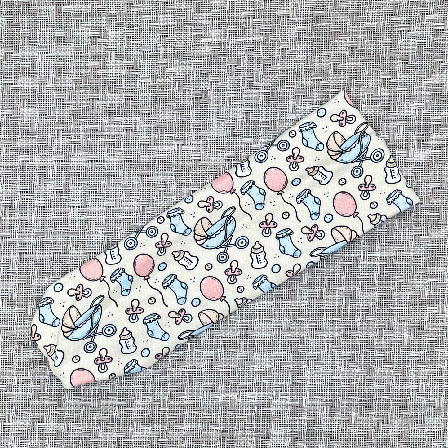 Baby-themed headband in cream color with blue, white, and pink on a textured gray background.