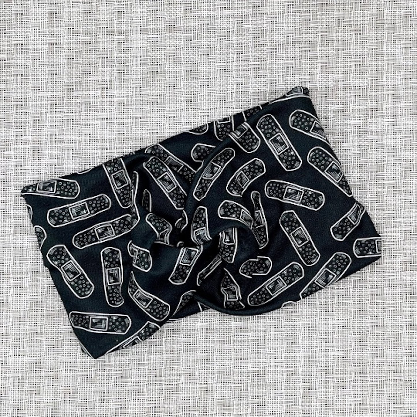 Wide, twisted headband in black with white bandage print.