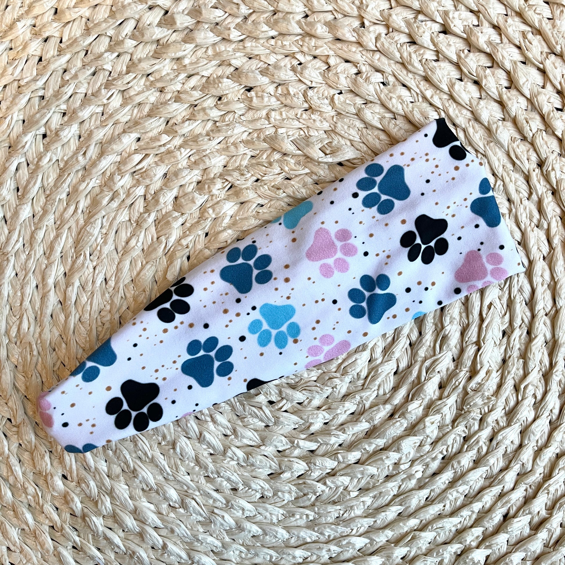Flat, stretchy headband in white with blue and pink dog paw print.