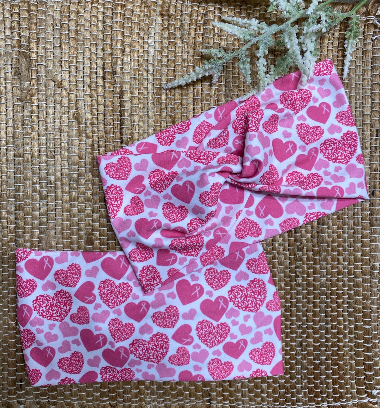 Wide, twisted headband in white with pink heart and pink ribbon print.
