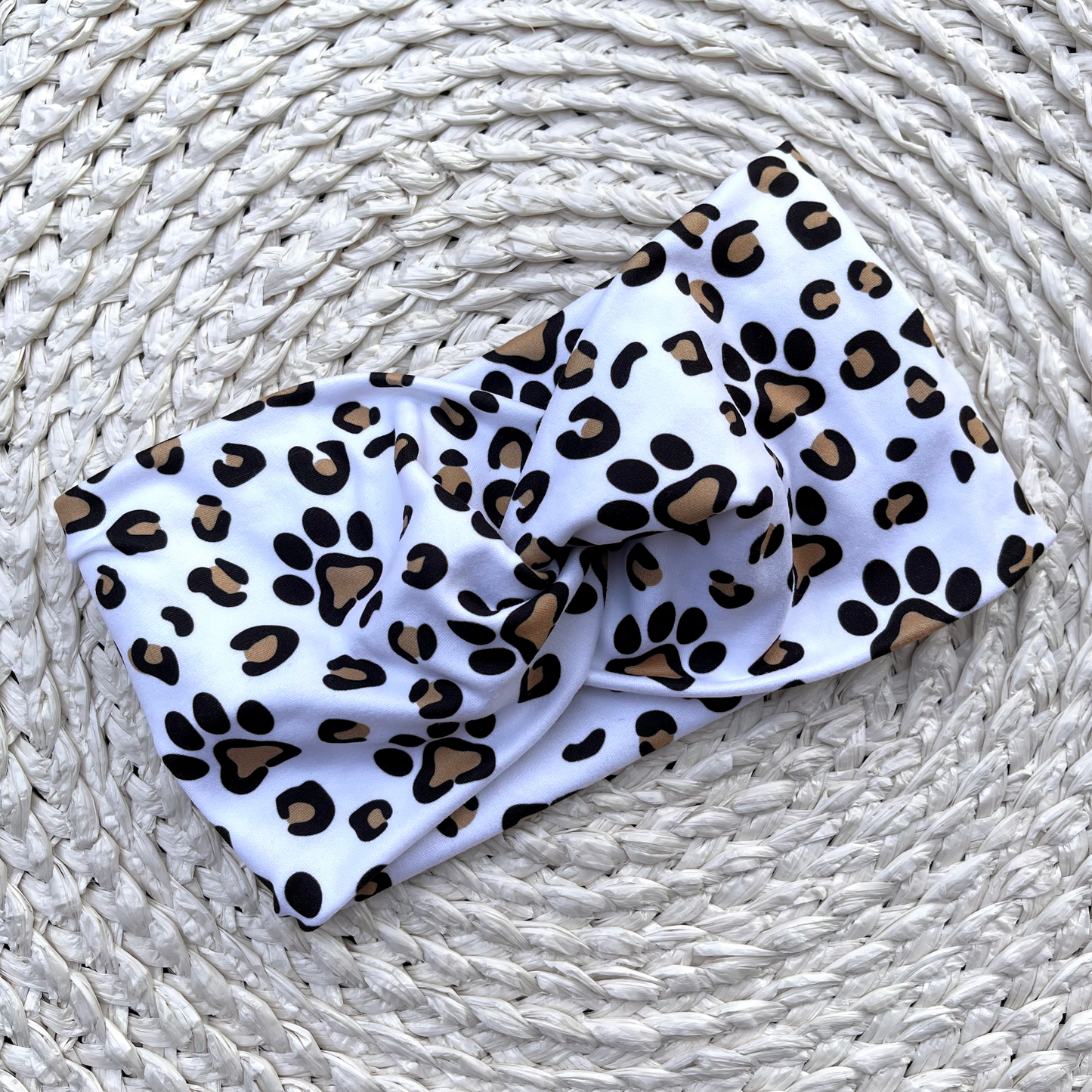 Wide, white, twisted headband with brown and black dog paws and cheetah print.
