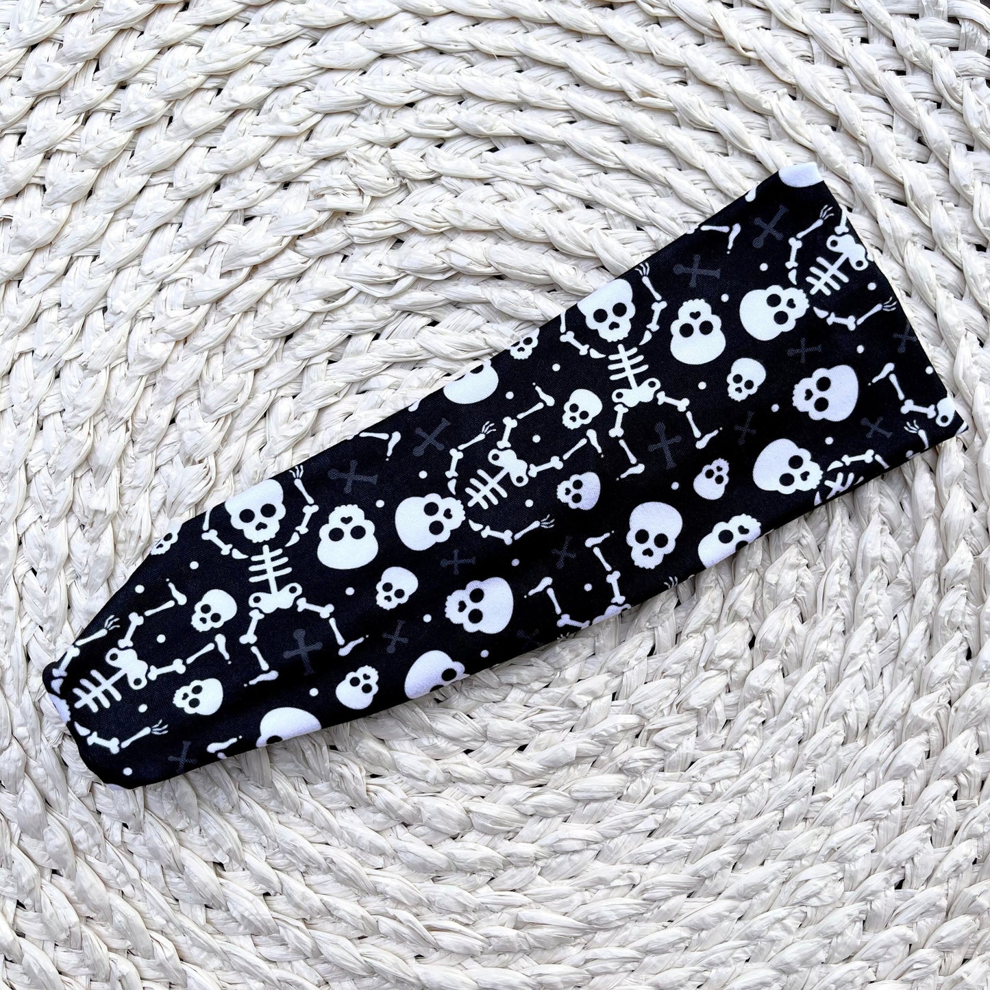 Black headband with white skull and skeleton pattern on a woven white surface