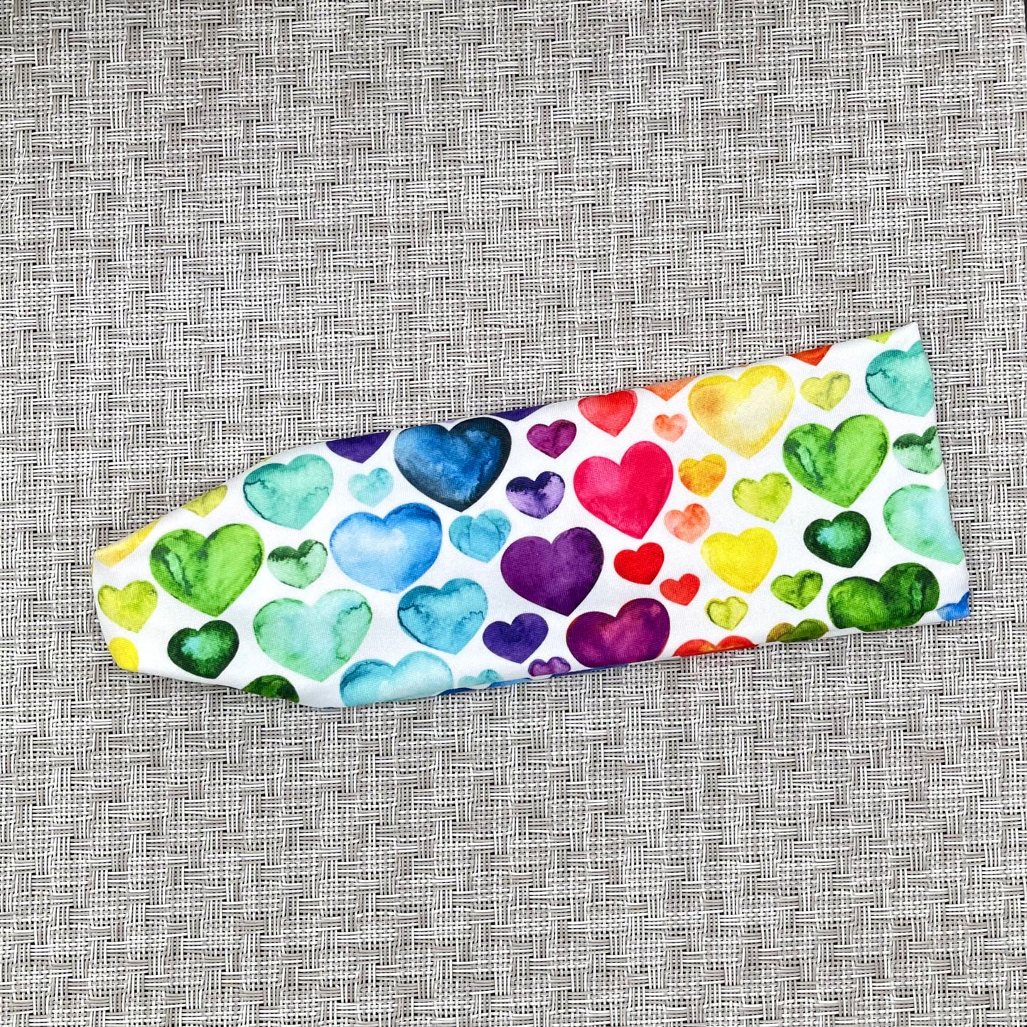 Flat, stretchy headband in white with rainbow heart print.