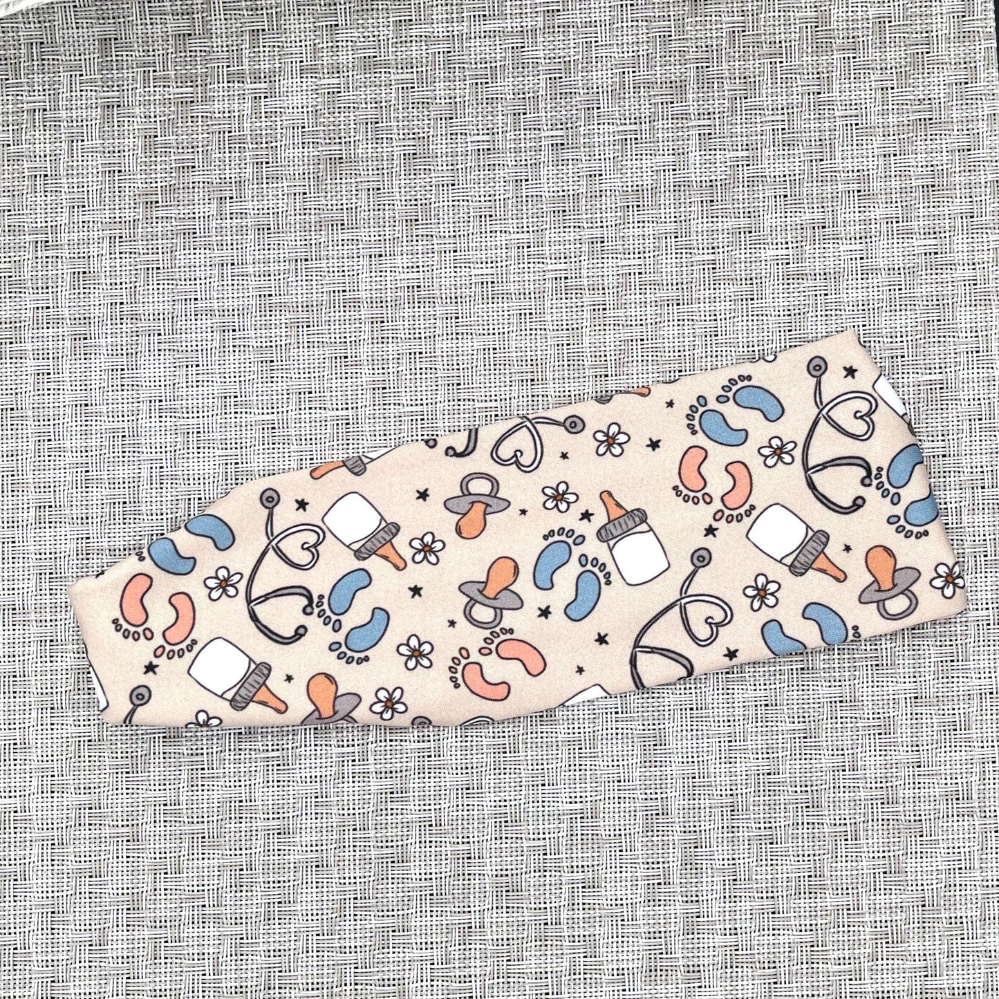Tan headband with baby-themed pattern on a textured gray background