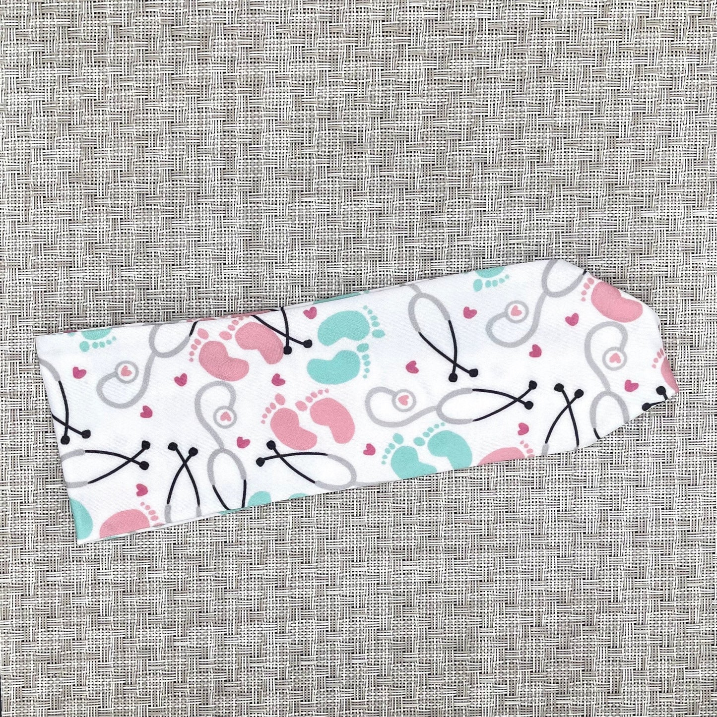 Baby-themed headband with stethoscope, footprints, and hearts on a gray background