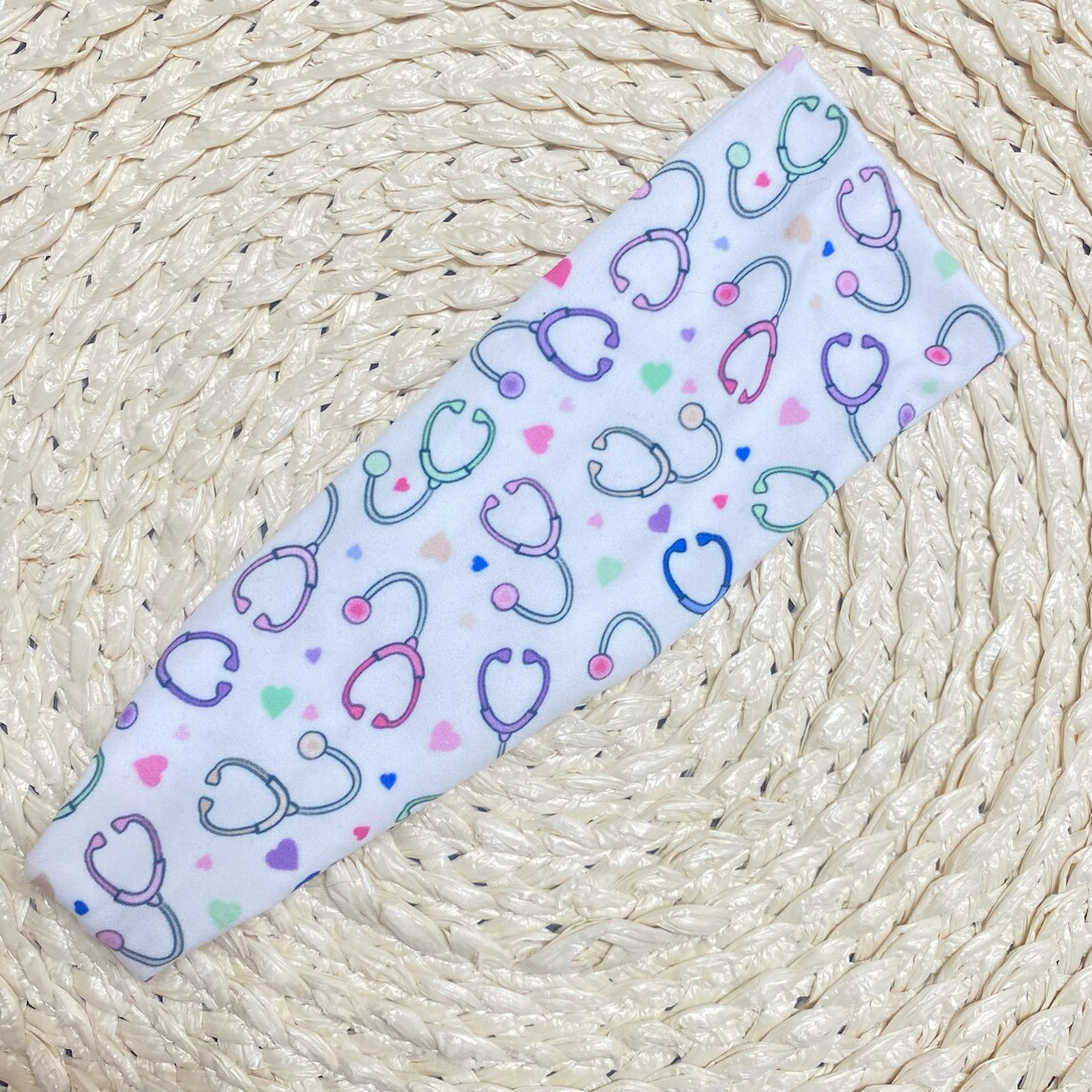Flat, stretchy, white headband with pastel color stethoscope and heart print.
