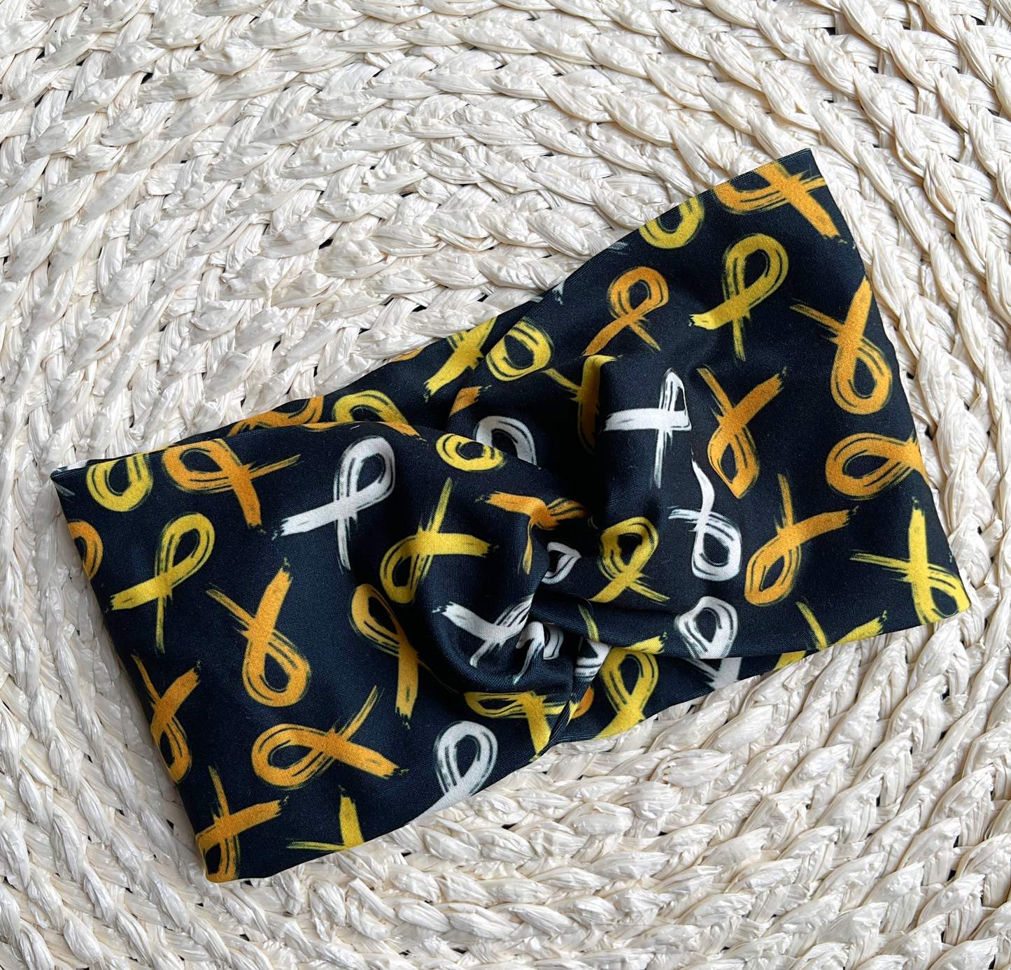 Black, wide, twisted headband with gold ribbon print.