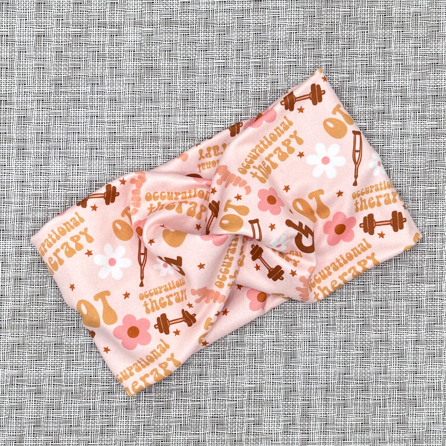 Wide, twisted, pink headband with print- OT, occupational therapy with flowers, crutches, a wheelchair, and weights.