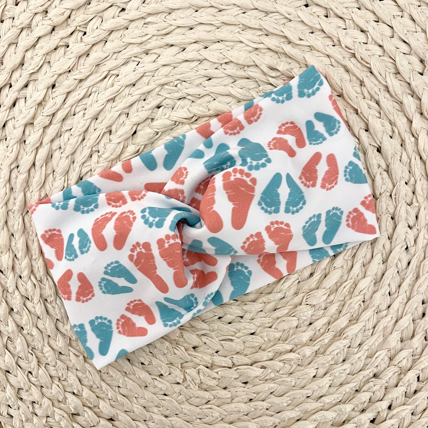 Wide, twisted headband in white with pink and blue baby feet print.