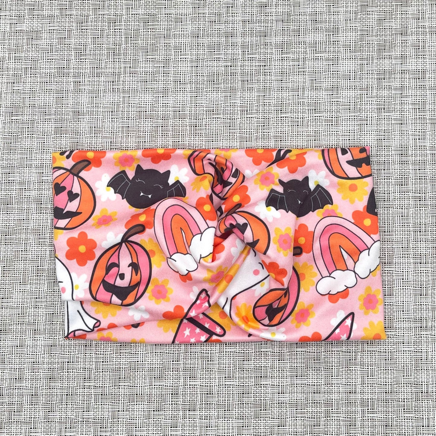 Wide, twisted headband in pink with floral, rainbow, and halloween print in pink, white, black, yellow, and orange.