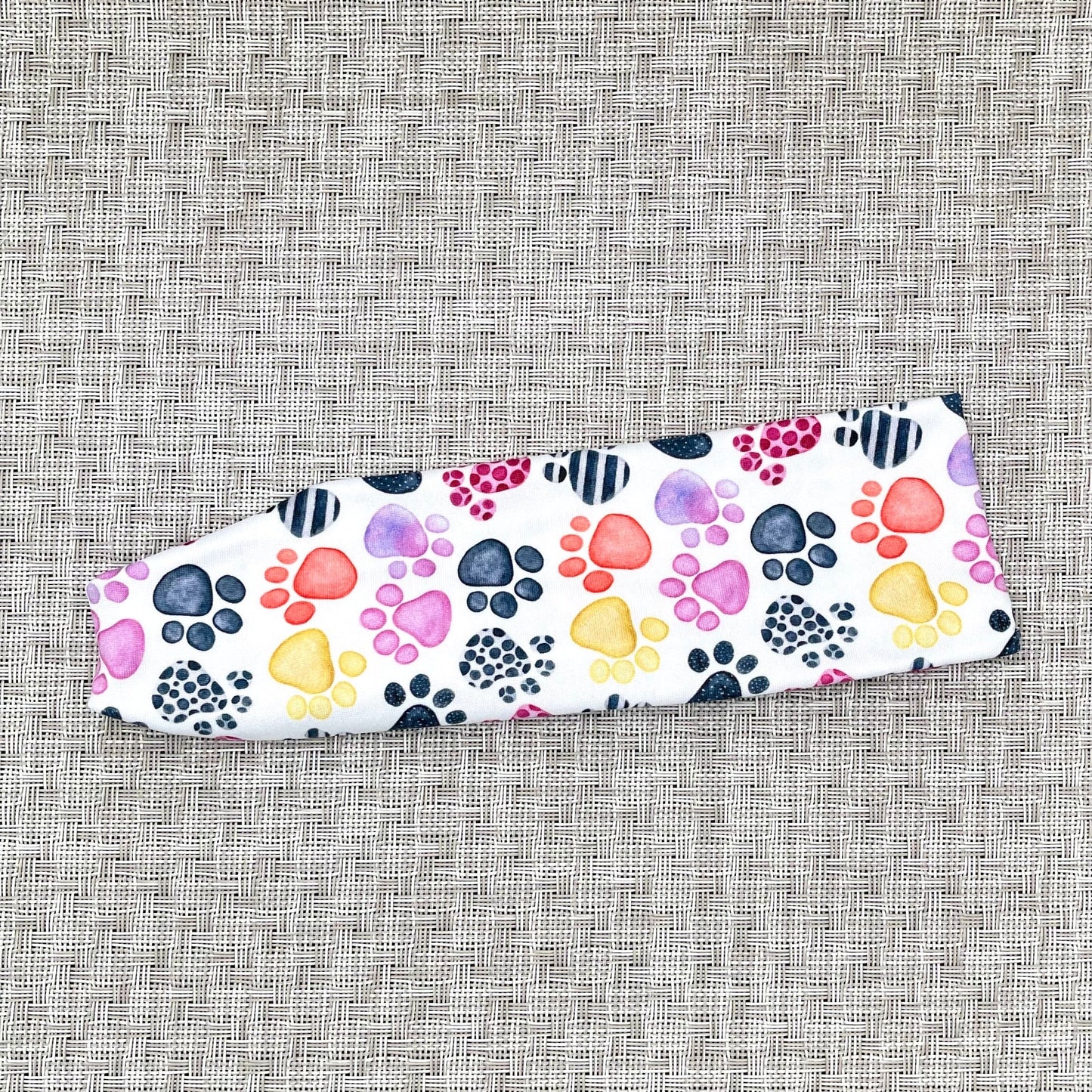 Flat, stretchy, white headband with multi-color dog paw print.