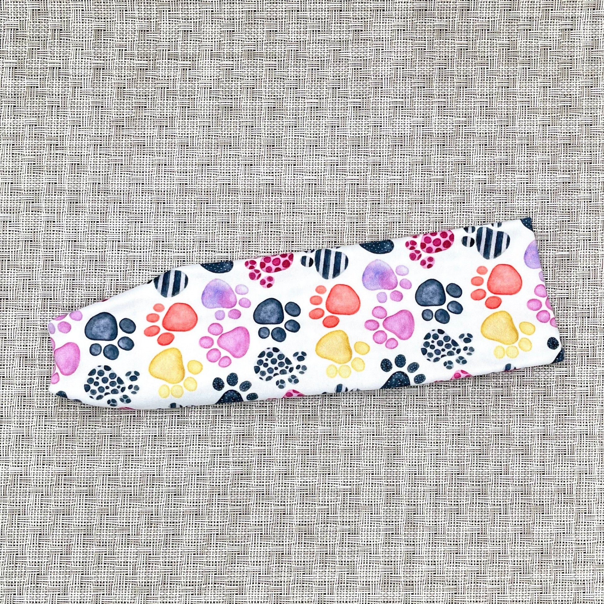 Flat, stretchy, white headband with multi-color dog paw print.