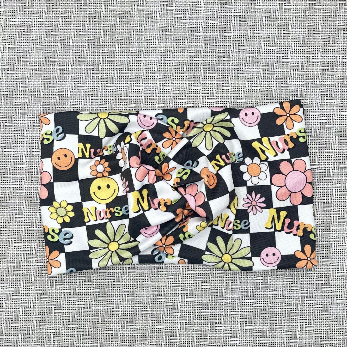 Black and white checker print wide twist headband with "nurse" print and flowers in rainbow colors.