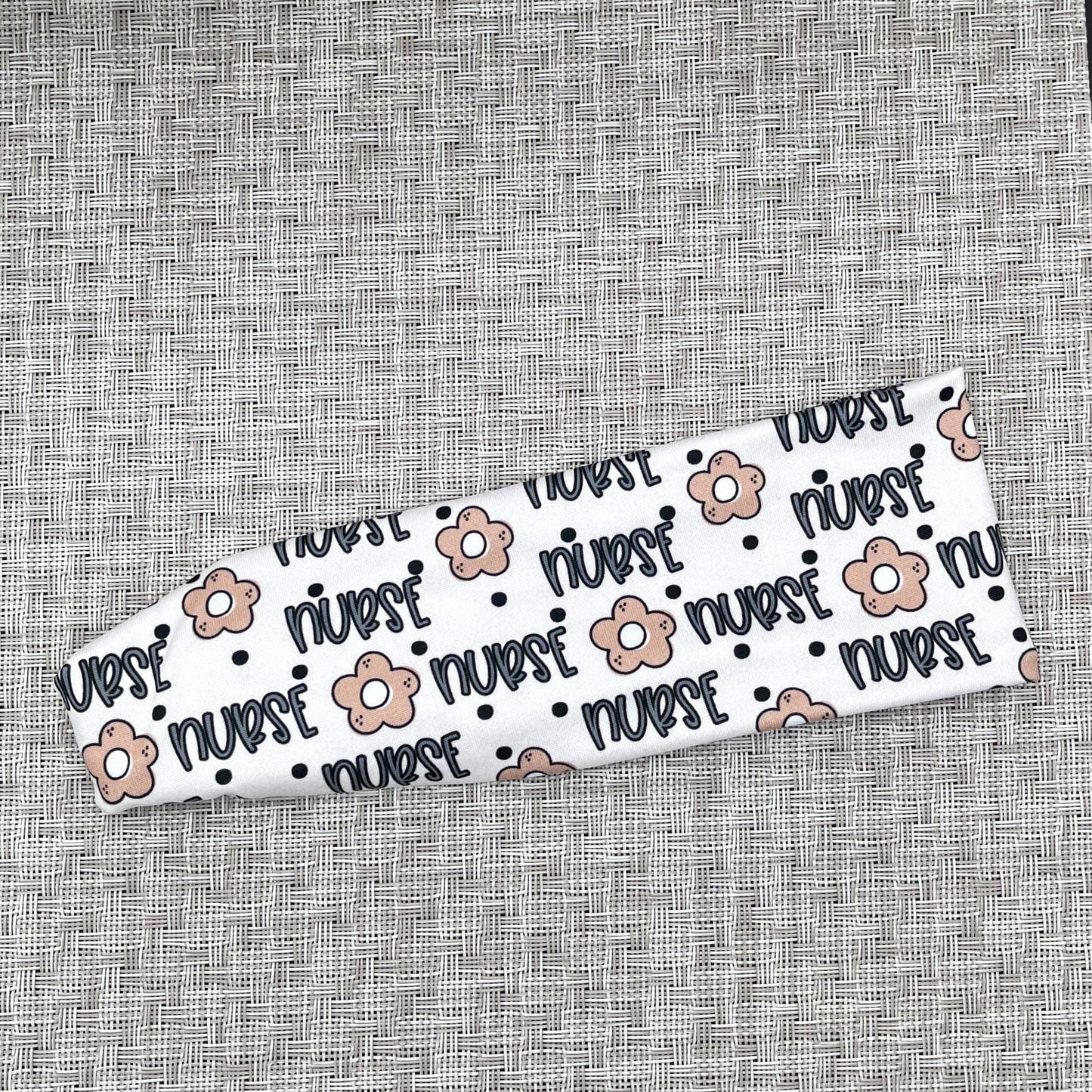 Flat, stretchy, white headband with "nurse", flowers, and polka dot print in blue and tan.