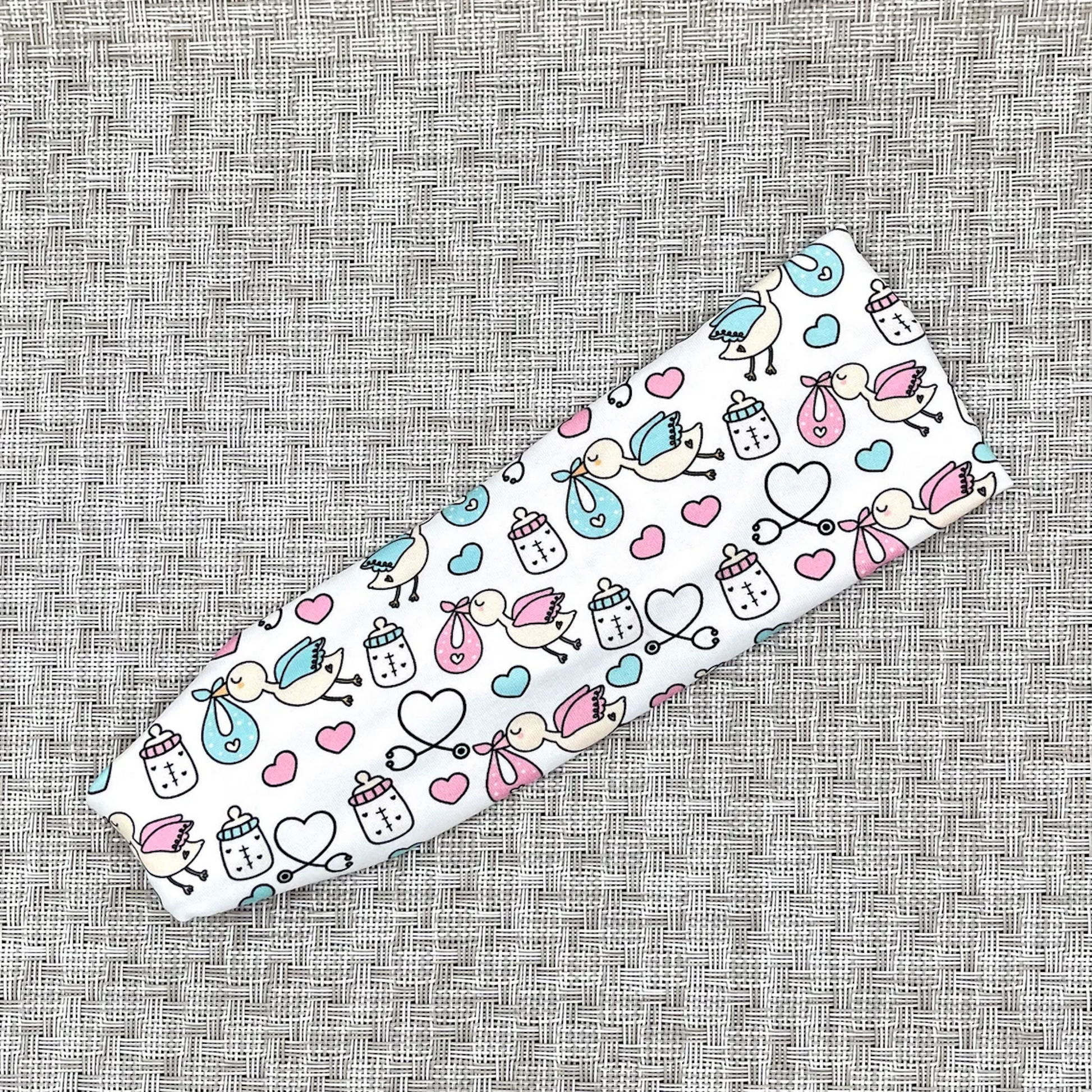 White, stretchy headband with baby theme print- storks, hearts, bottles, and stethoscopes.