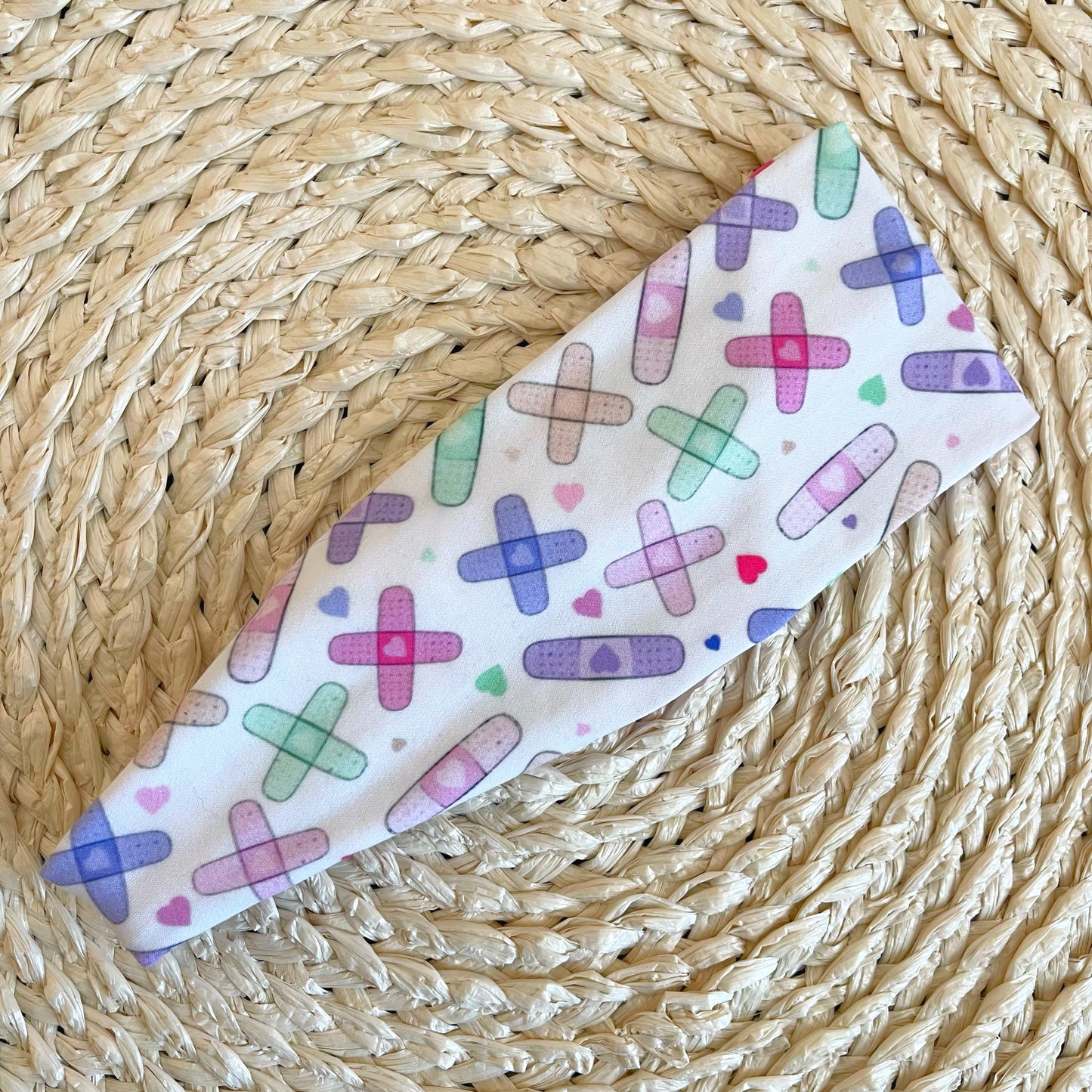 White, stretchy headband with pastel color bandages print.