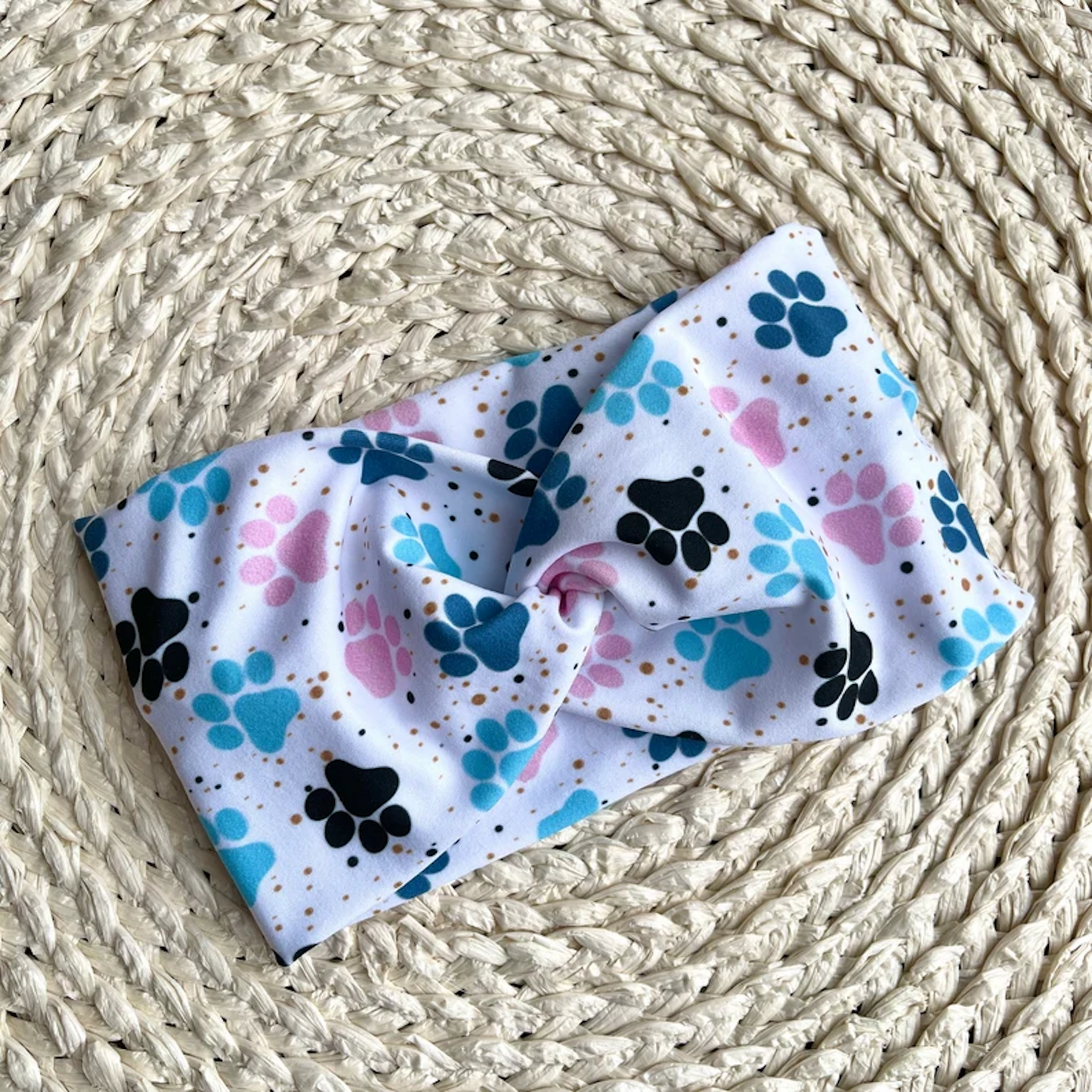 Wide, twisted headband in white with blue and pink paw prints.