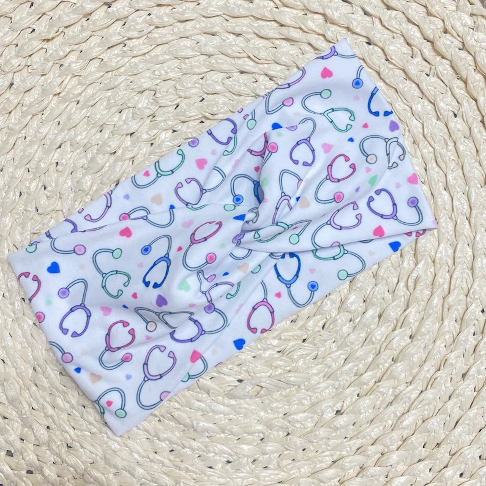 Wide, twisted, white headband with pastel color stethoscope print.