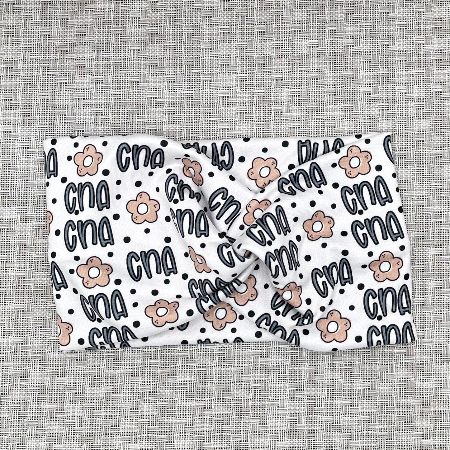 Wide, stretchy, cream color twisted headband with "CNA" print and polka dots in blue and tan flowers.