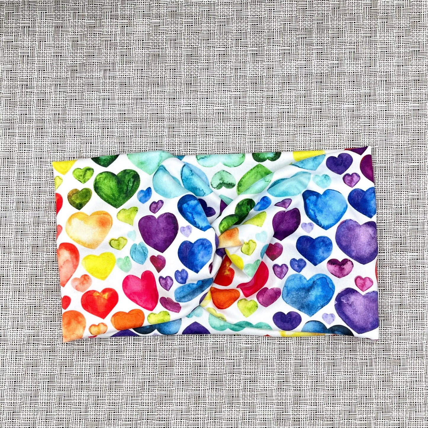Wide, twisted, white headband with rainbow heart print.