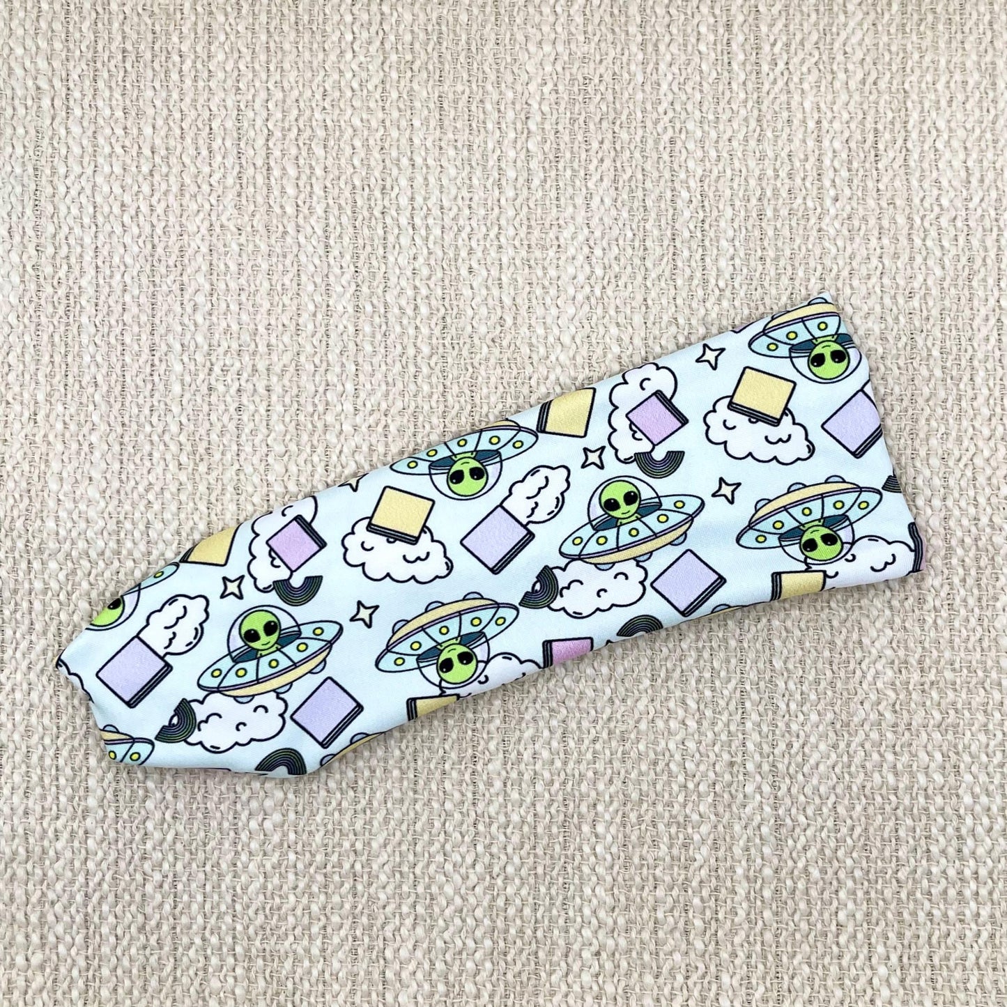 Flat, stretchy, light blue headband with alien and space theme print.