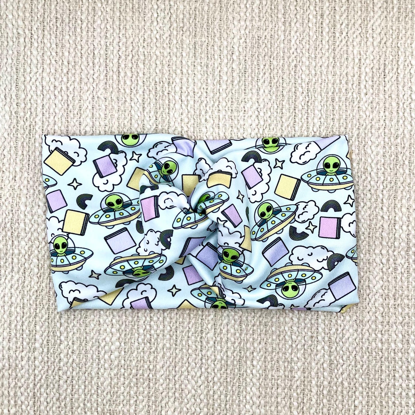 Wide, twisted, light blue headband with alien theme print.