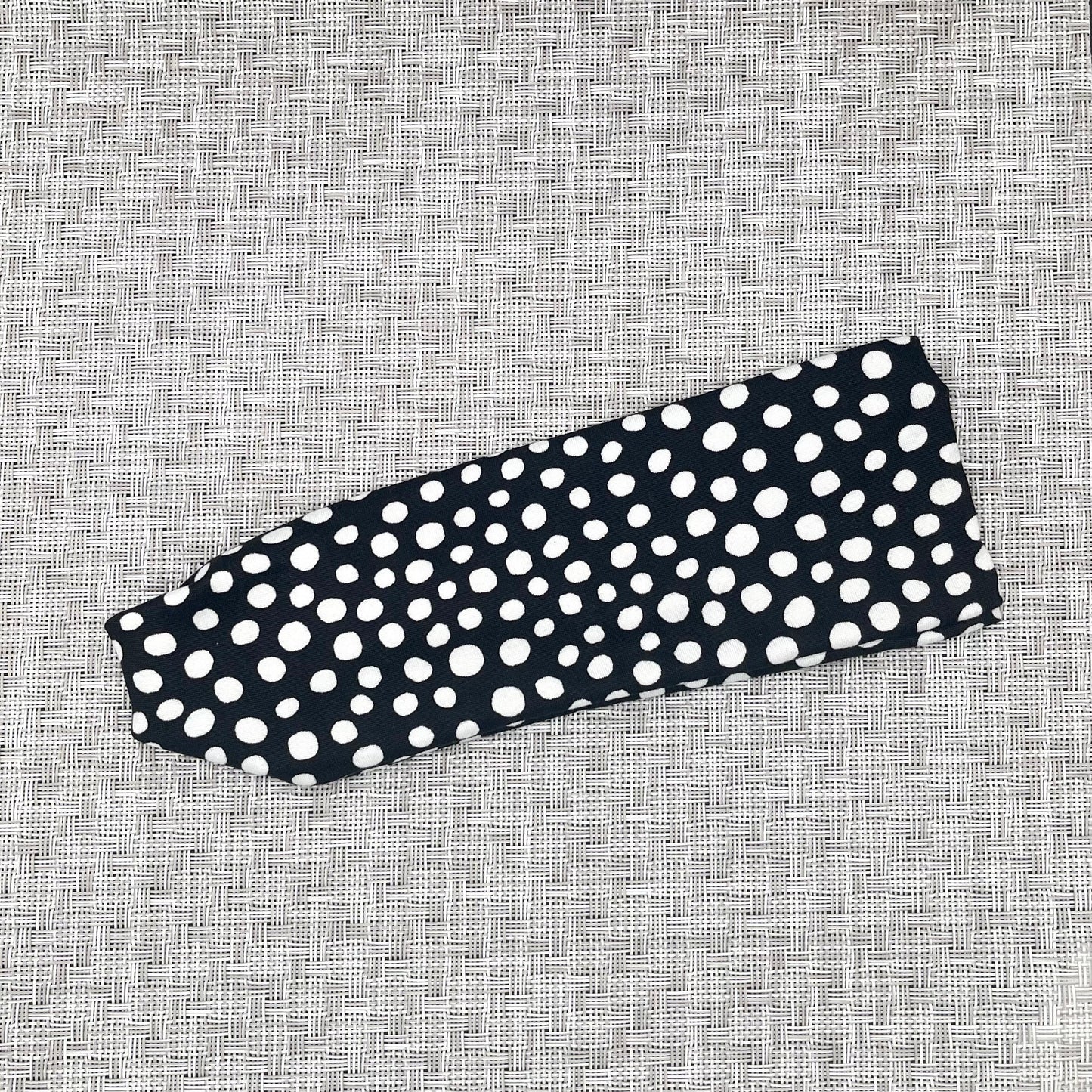 Flat, stretchy headband in black with white polka dot print.