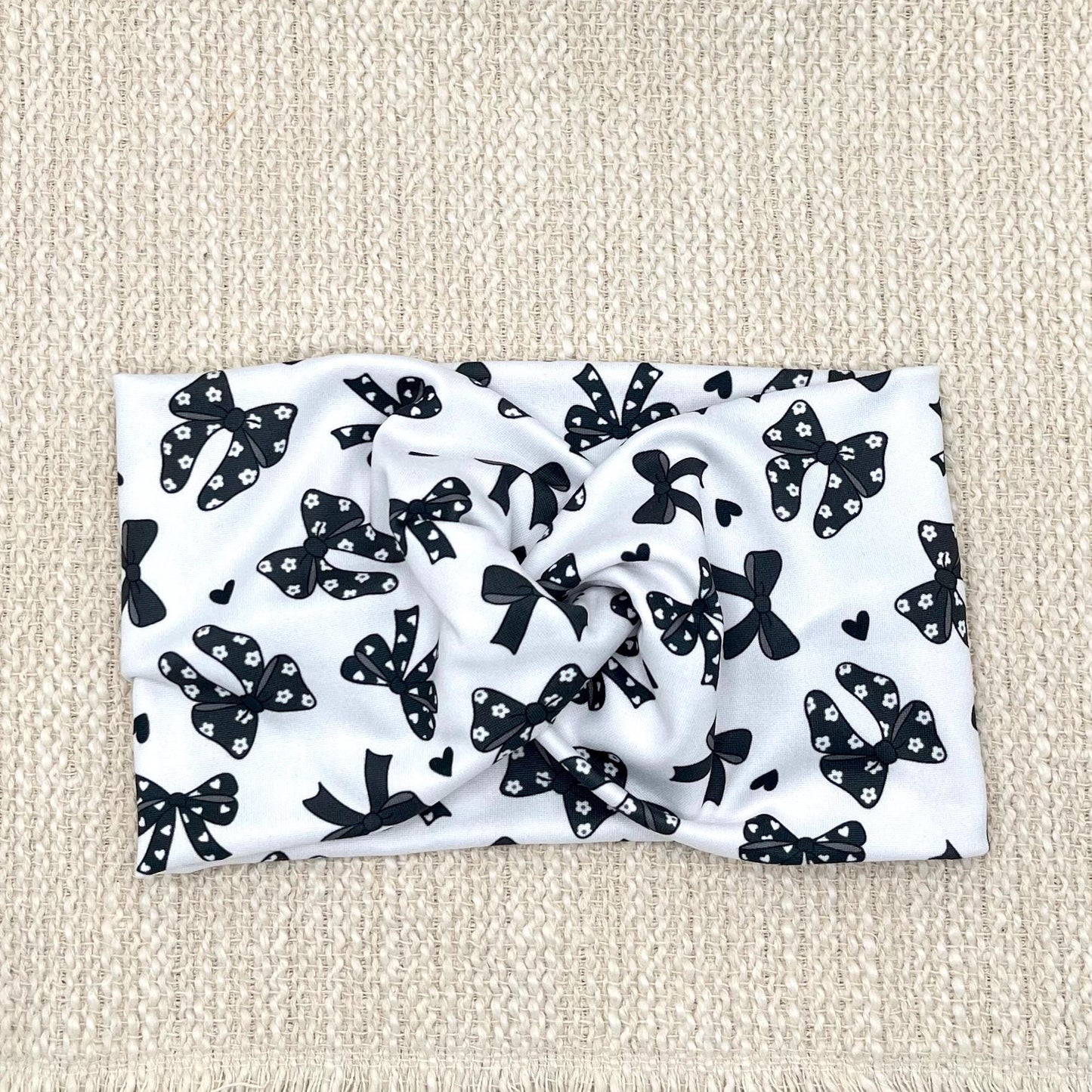 Wide, twisted, white headband with black bow print.