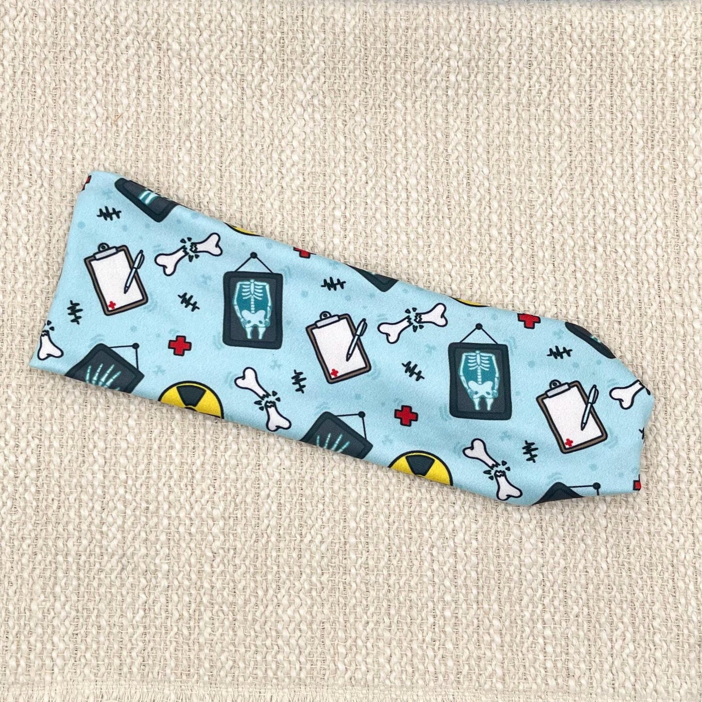 Flat, stretchy, blue headband with radiology theme print displayed on a cream background.