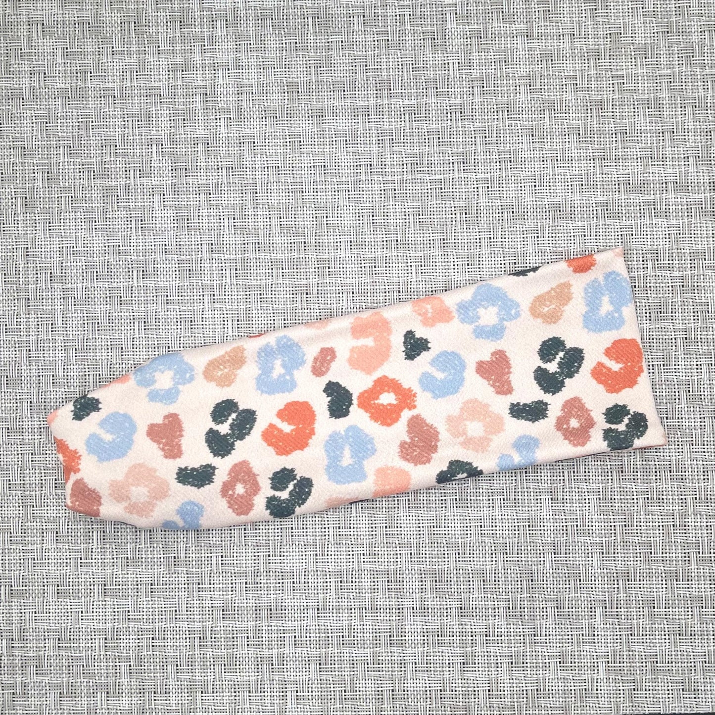Flat, stretchy headband in cream color with cheetah print in varying shades of blues, orange/peach, and tan.