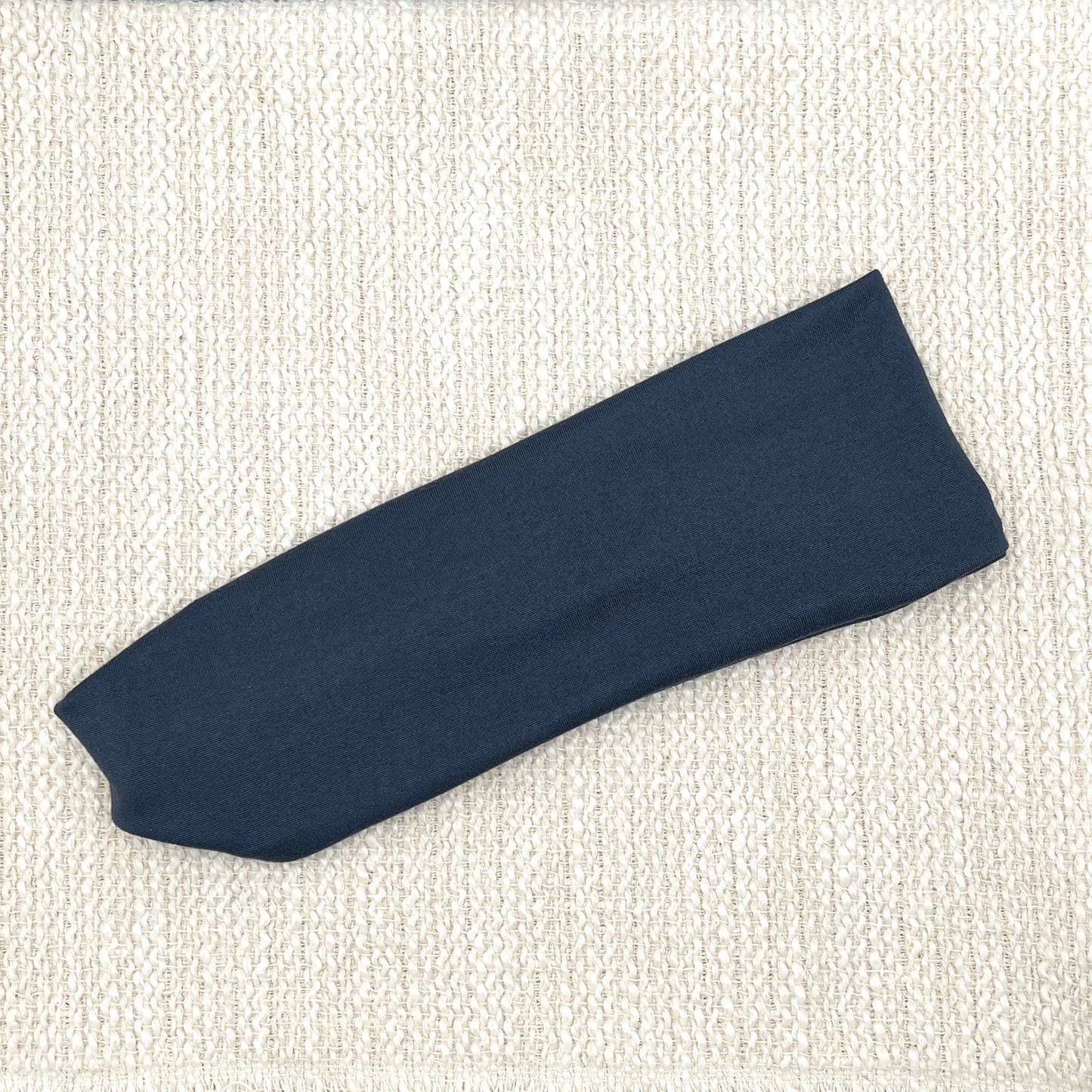 Flat, stretchy headband in charcoal gray displayed on cream color background.