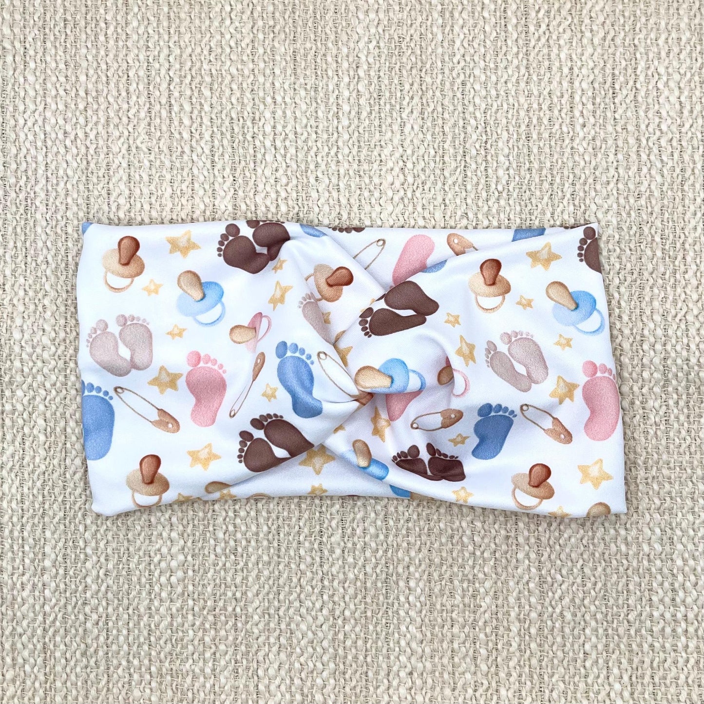 Wide, twisted, white headband with baby feet and baby theme print.