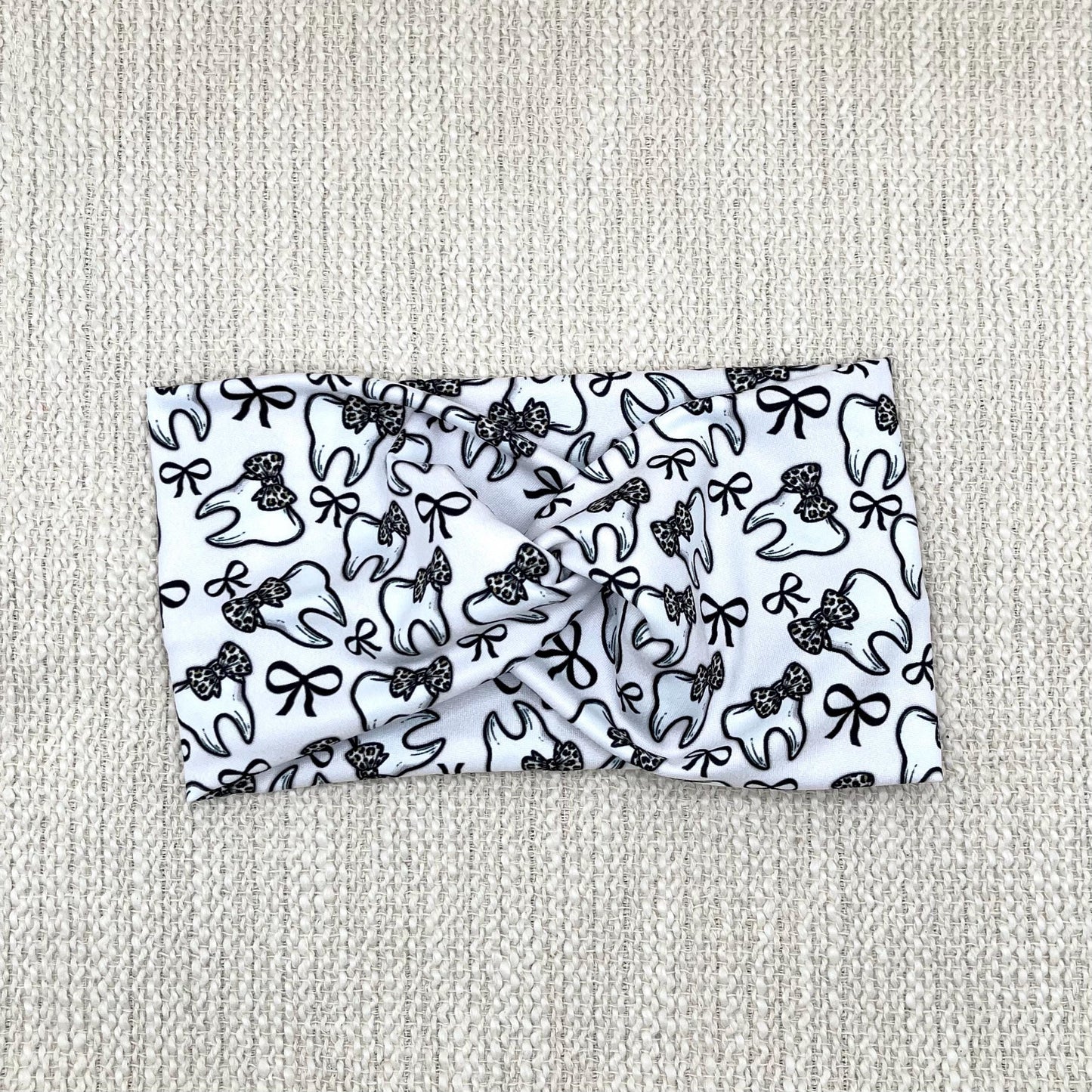 Wide, twisted, white headband in white with teeth and bow print in black and cheetah print.