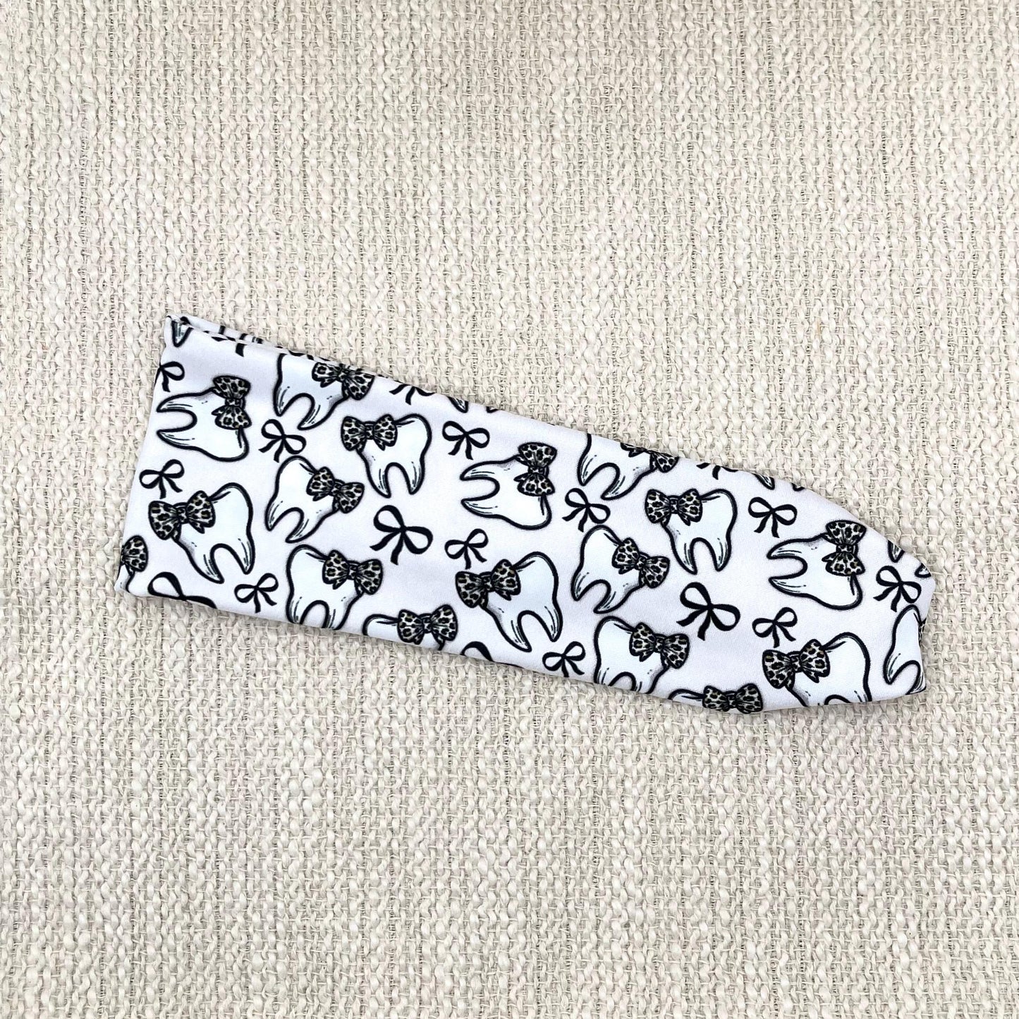 Flat, stretchy, white headband with teeth, bow, and leopard bow print.