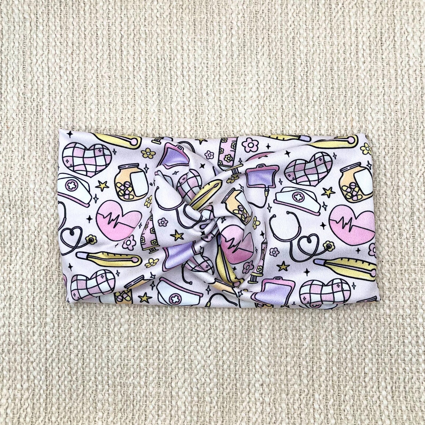 Wide, twisted headband with yellow, purple, and pink disco and medical theme print.