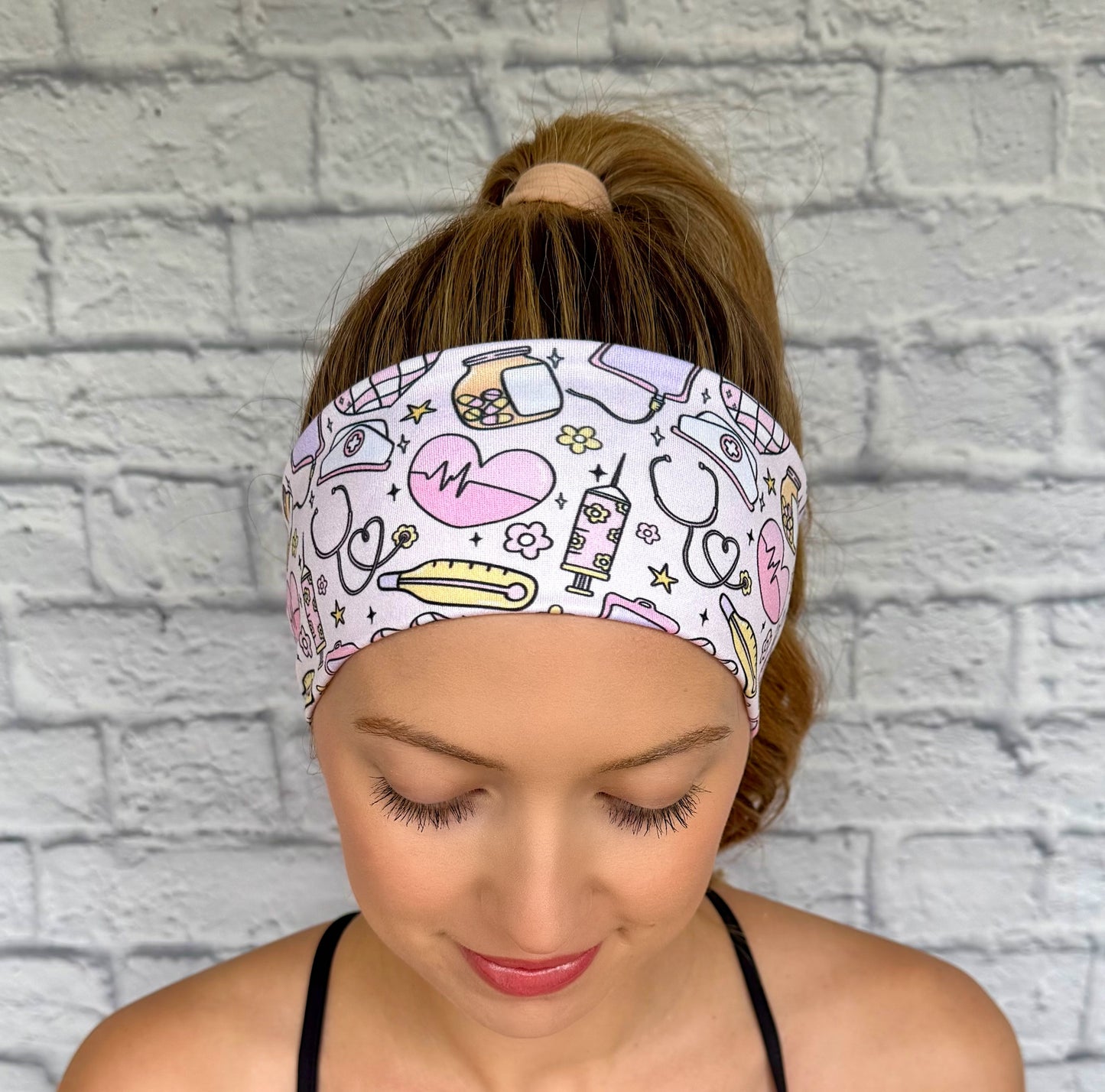Woman with hair in ponytail wearing flat, stretchy headband with medical, disco, and floral theme print mixed throughout fabric.
