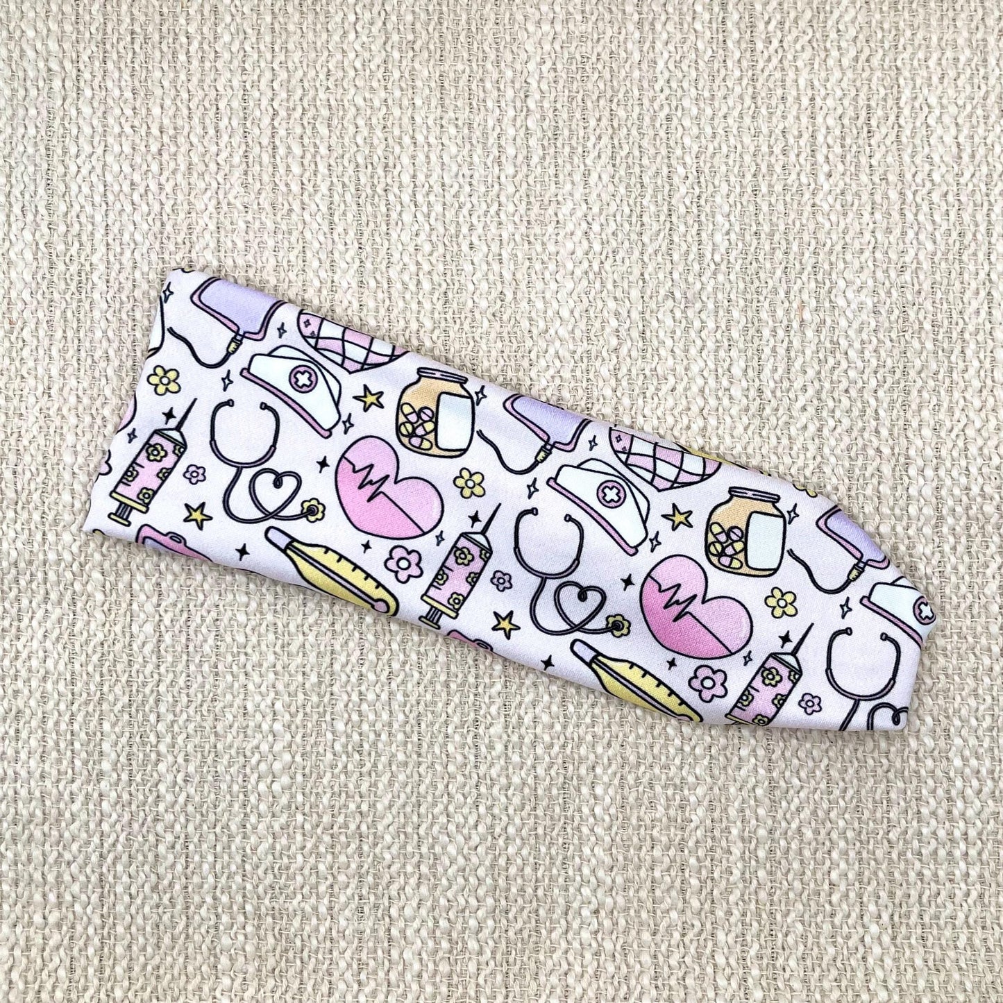 Flat, stretchy headband with medical, disco, and floral theme print mixed throughout fabric.
