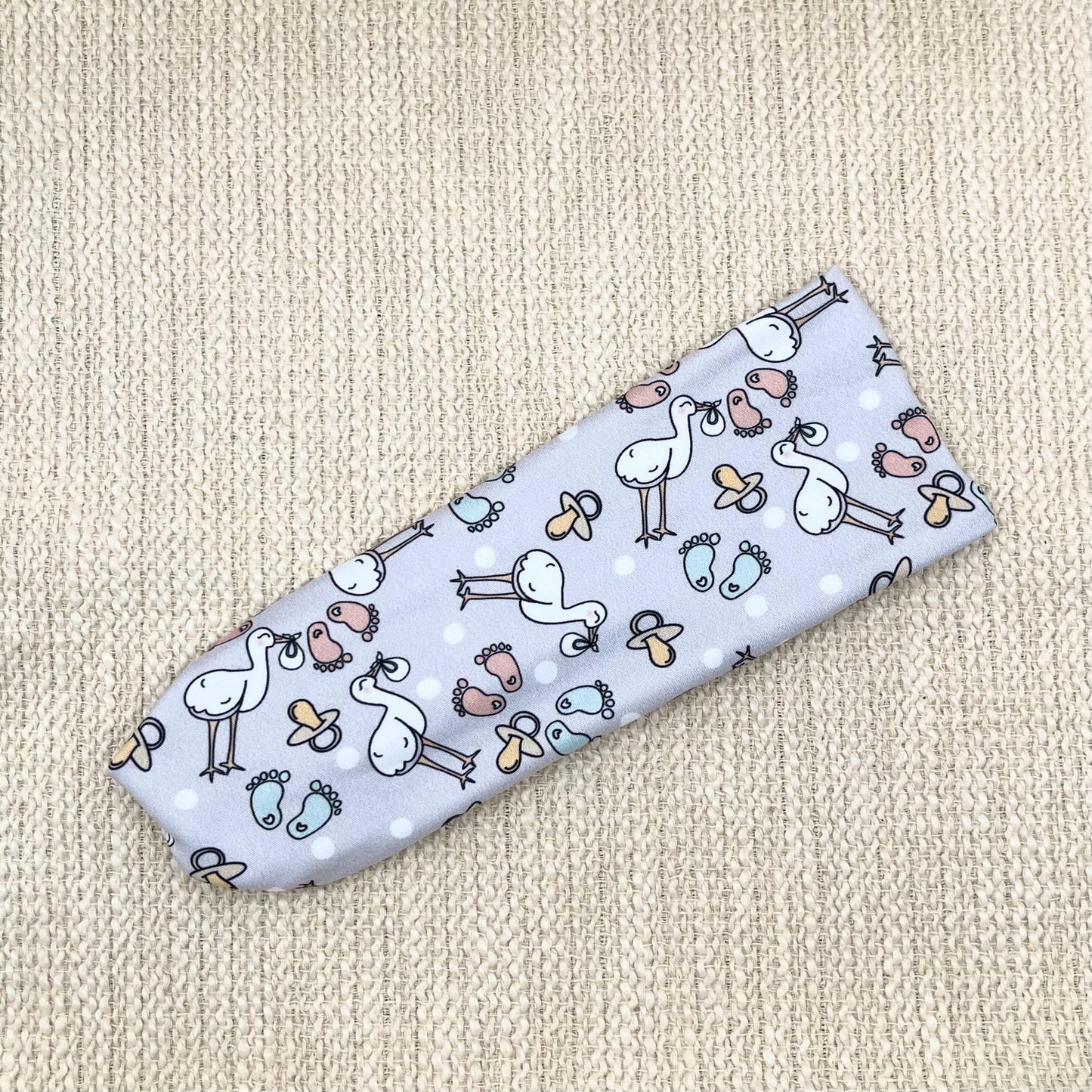 Flat, stretchy, light gray headband with stork and baby theme print.