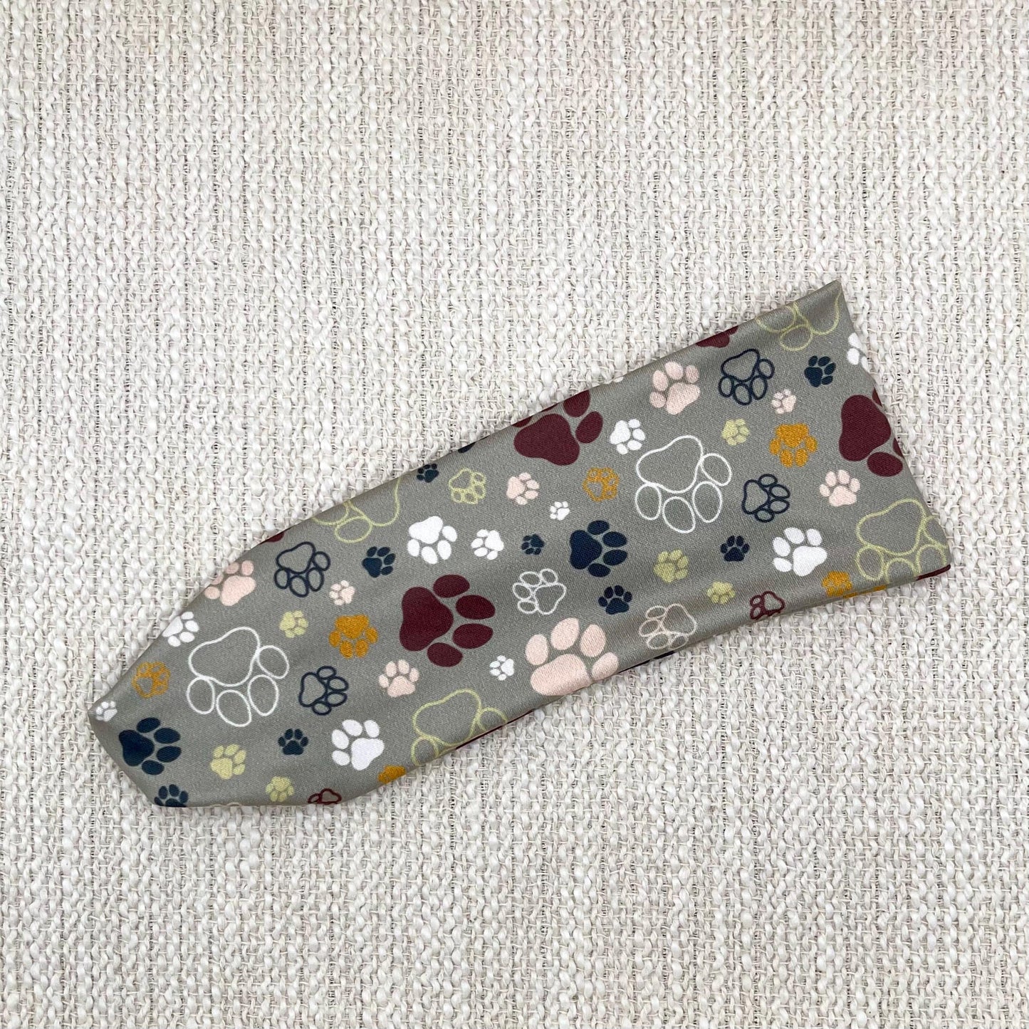 Flat, stretchy, light green headband with multi-color dog paw print.