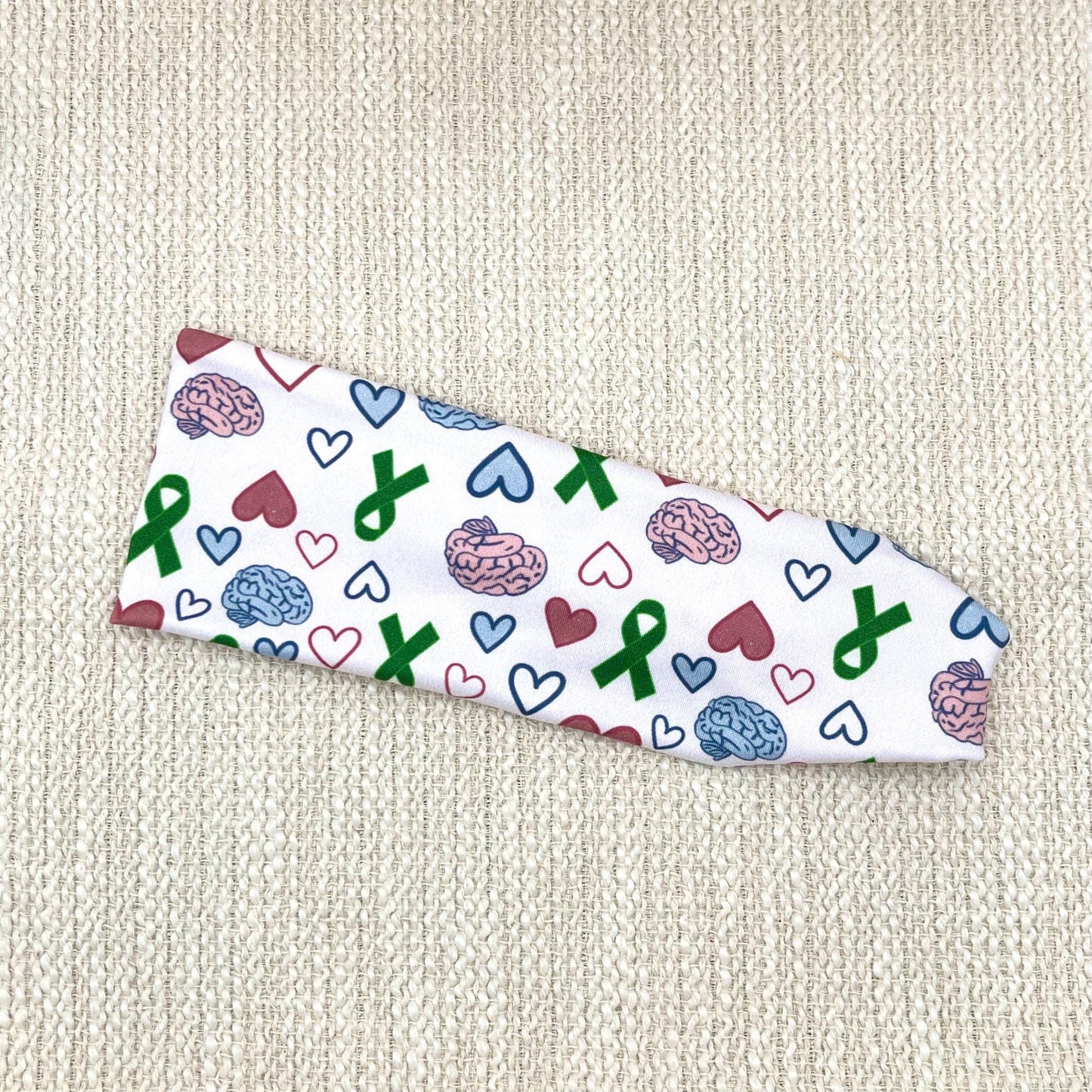 Flat, stretchy headband with green ribbon, pink and blue brain, and pink and blue heart print.